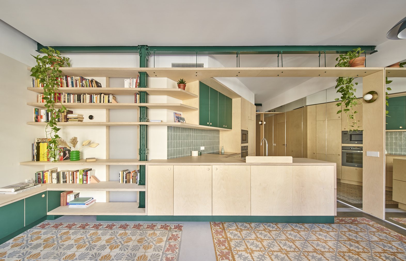 Cocina moderna con estanterías abiertas, gabinetes verdes y azulejos verdes en la pared, pisos con azulejos decorativos y plantas en macetas.
