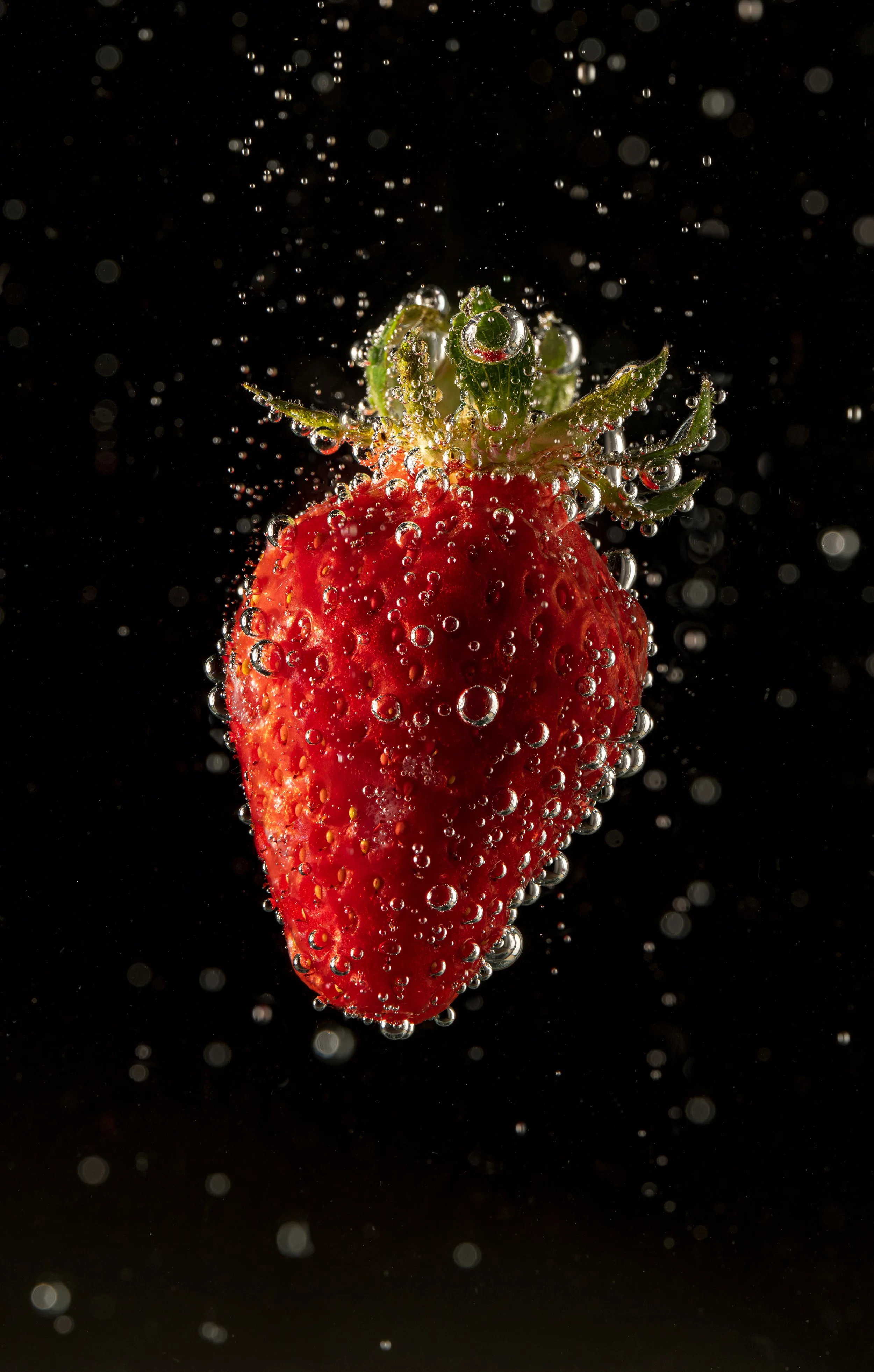 Fresh strawberry submerged in water with bubbles against a dark background.