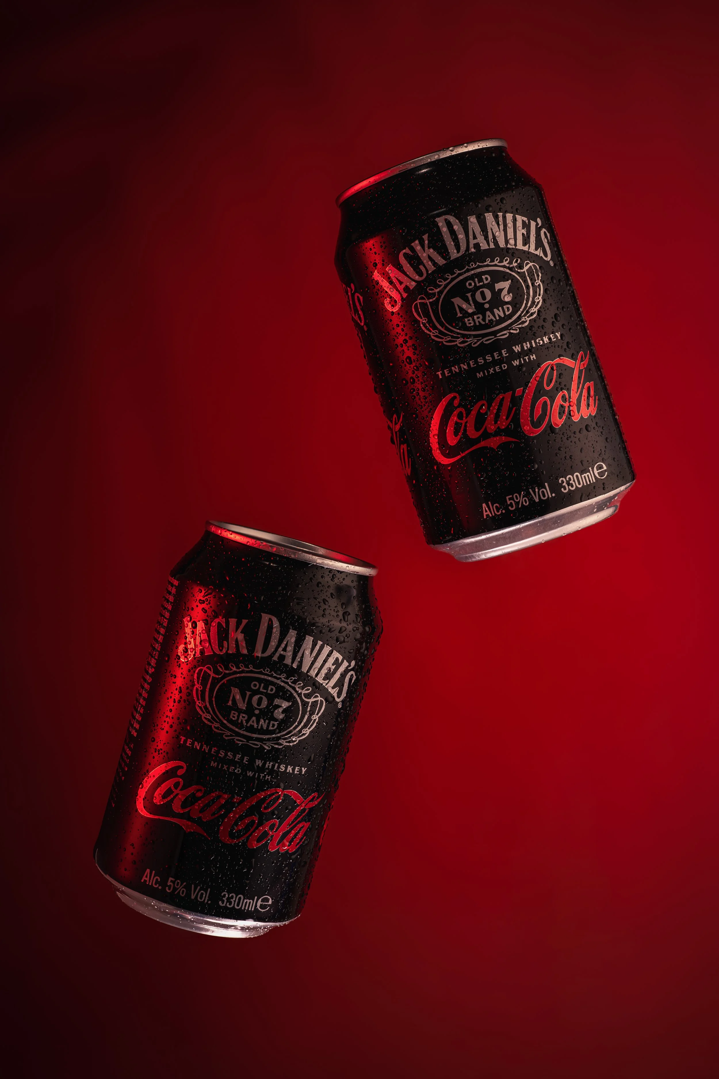Jack Daniel’s & Coca-Cola cans photographed with dramatic red lighting and suspended motion.