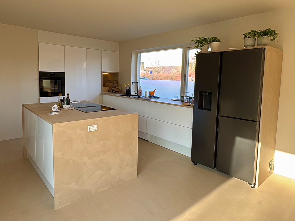 Modern kitchen with white cabinets, a kitchen island with a cooktop, black refrigerator, and a window with sunlight streaming in.