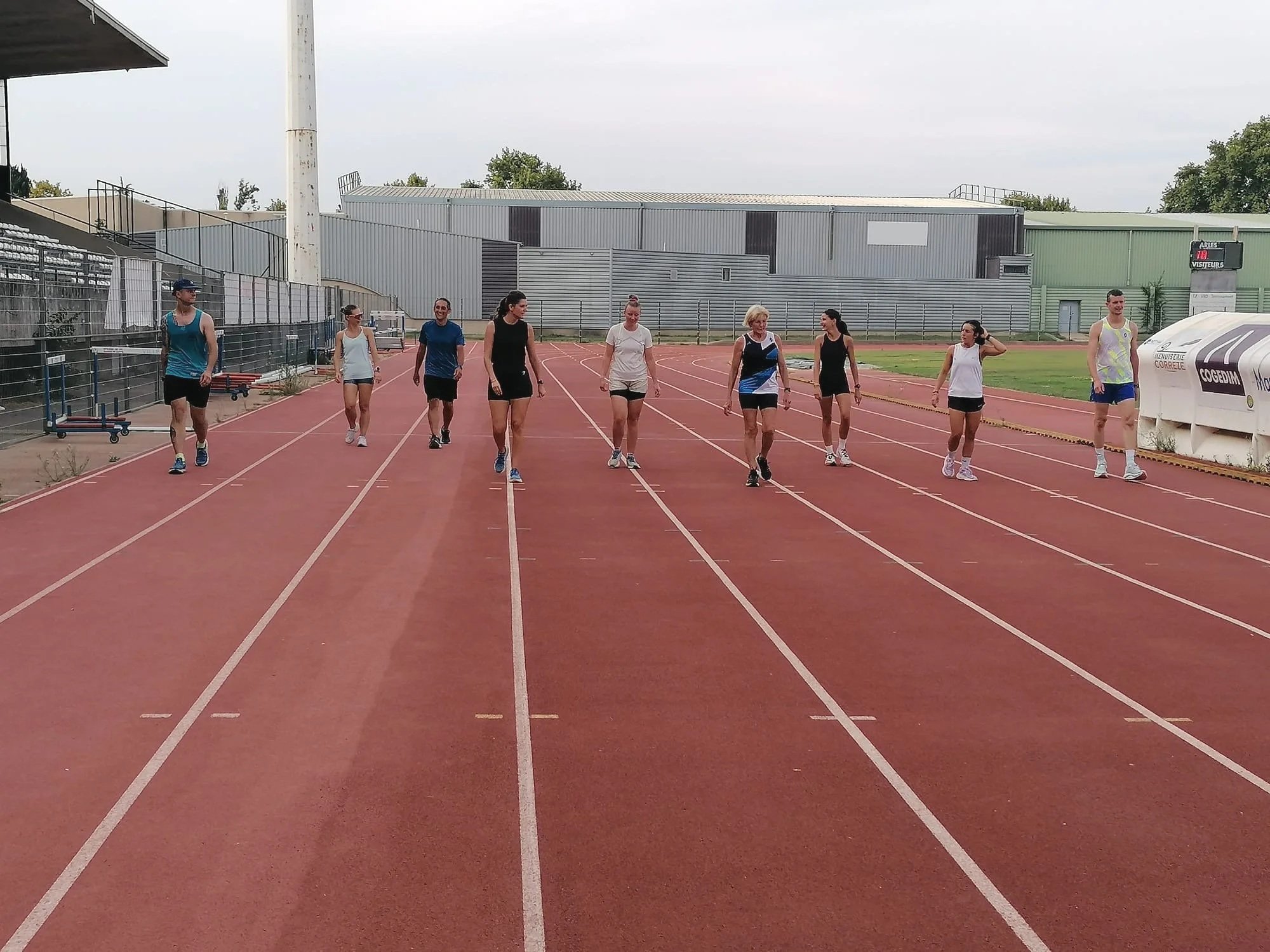 Groupe de personnes marchant ou se préparant à courir sur une piste d'athlétisme extérieure.