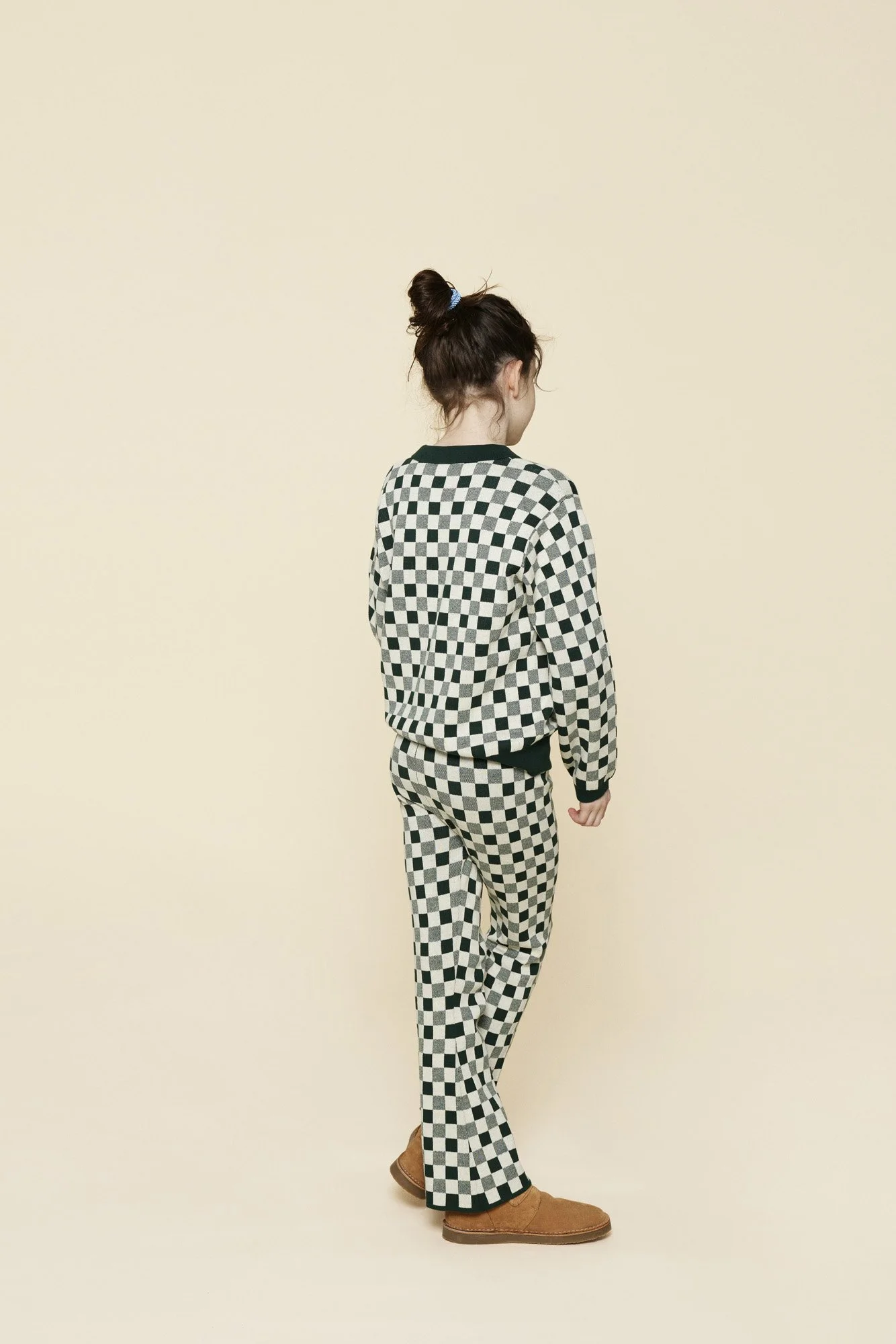 A woman seen from behind wearing a checkered black and white sweater and matching pants, standing against a plain, light-colored background.