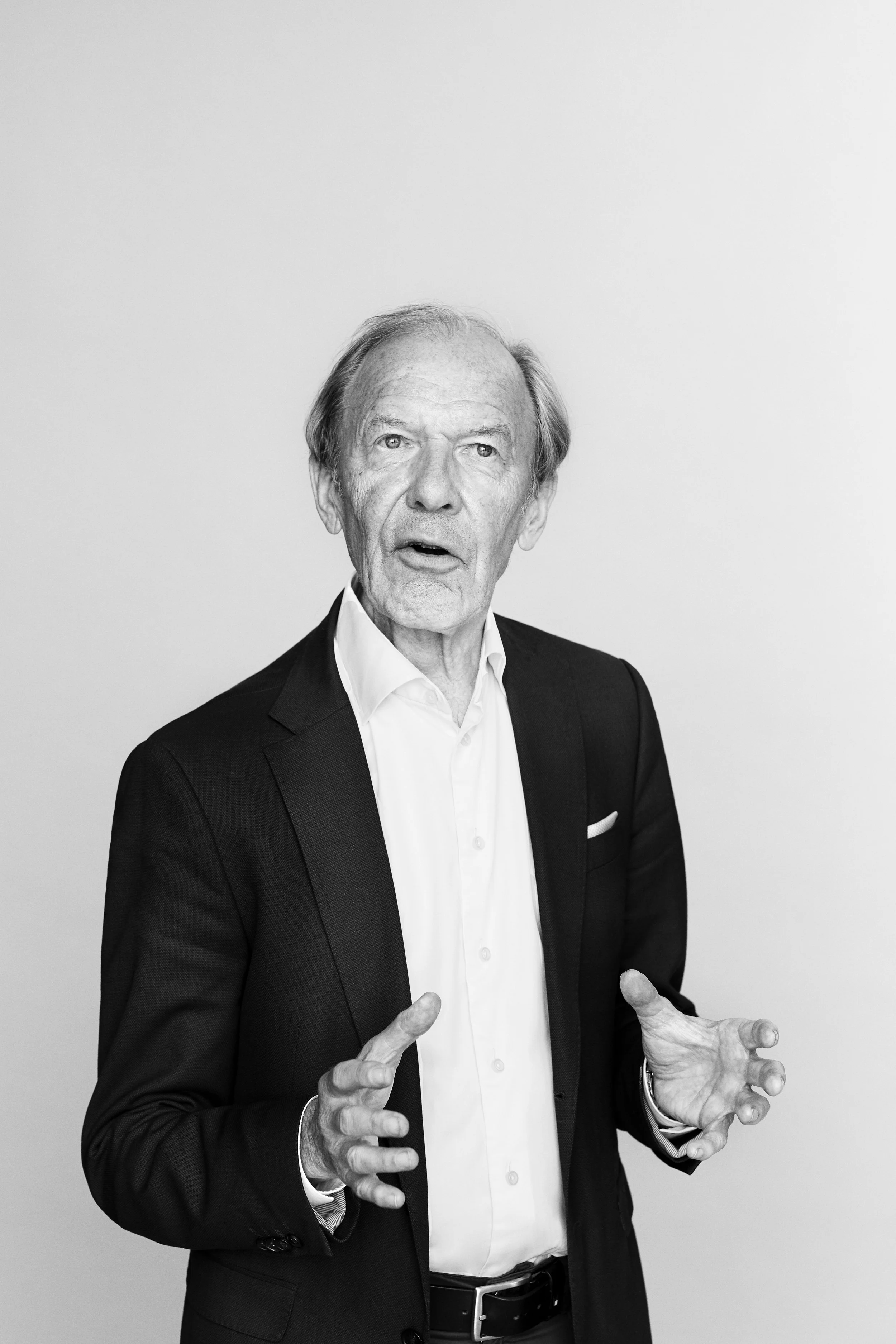 Black and white photo of an elderly man in a suit speaking and gesturing with his hands.