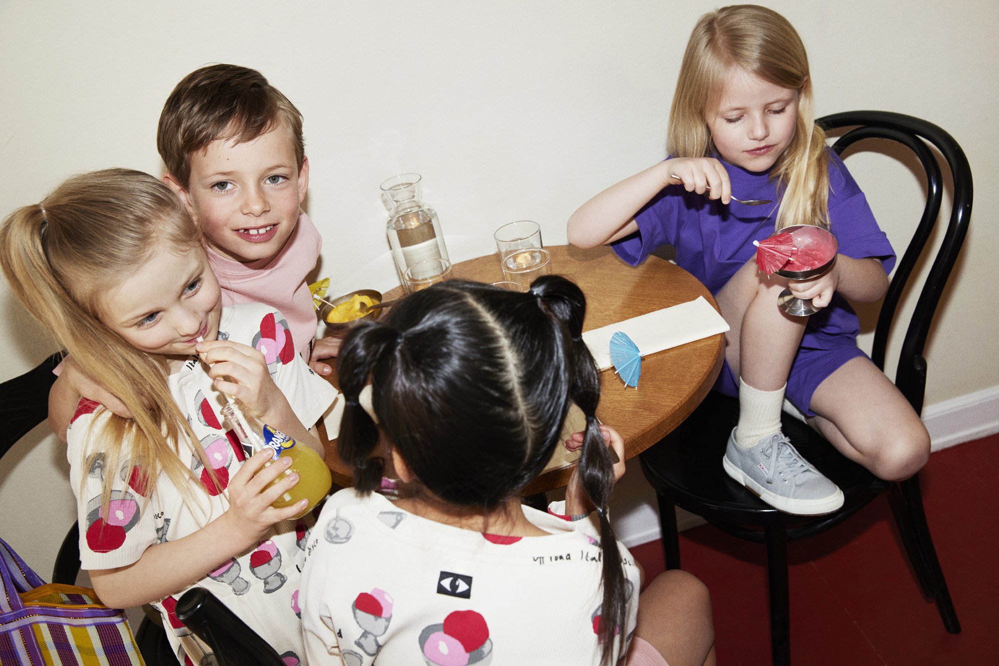 Four young girls sitting around a wooden table, enjoying drinks with colorful umbrellas at a snack party.