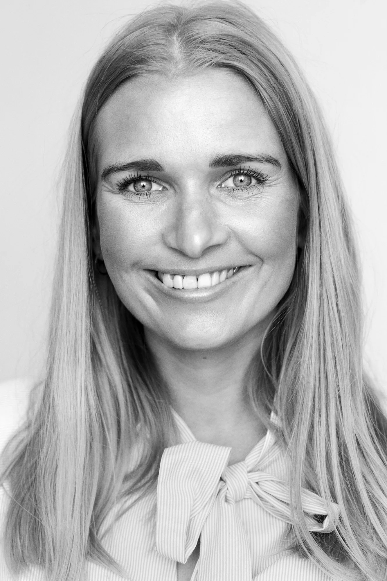 A smiling woman with long blonde hair, wearing a striped blouse with a bow tie.