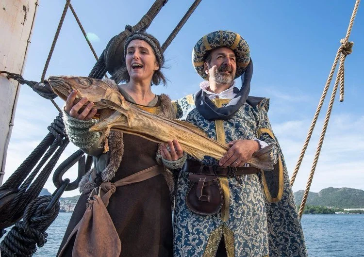 Un uomo e una donna vestiti con abiti storici che tengono in mano un pesce essiccato