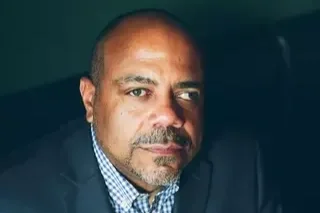 A man with short hair in a suit in front. of a dark backgroun