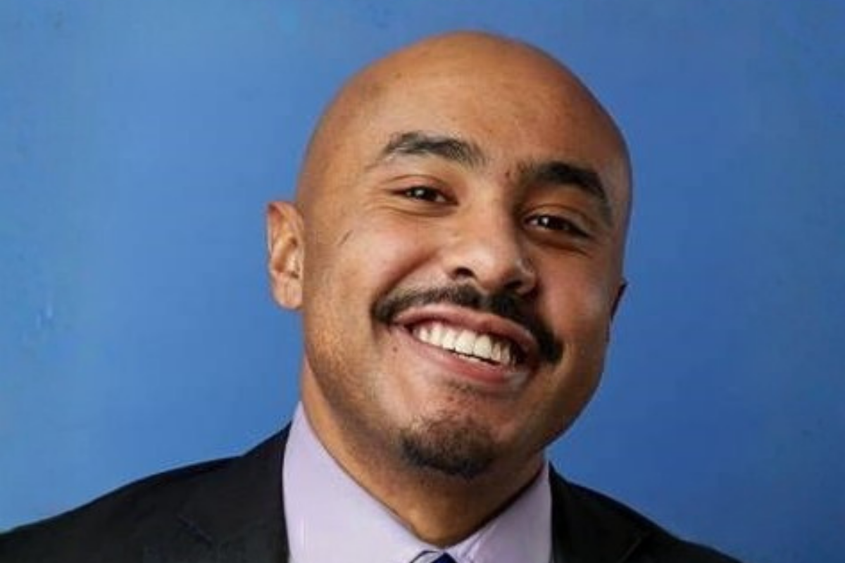 A man with a suit smiling in front of a blue background