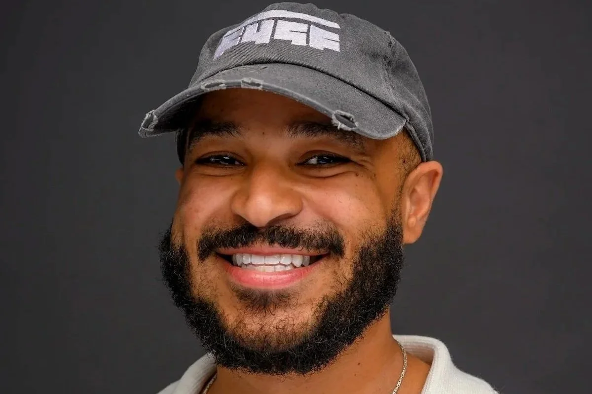 Smiling man with a beard and short hair sitting on a booth in a restaurant or cafe. F4GF Kareem Alston-Rosales