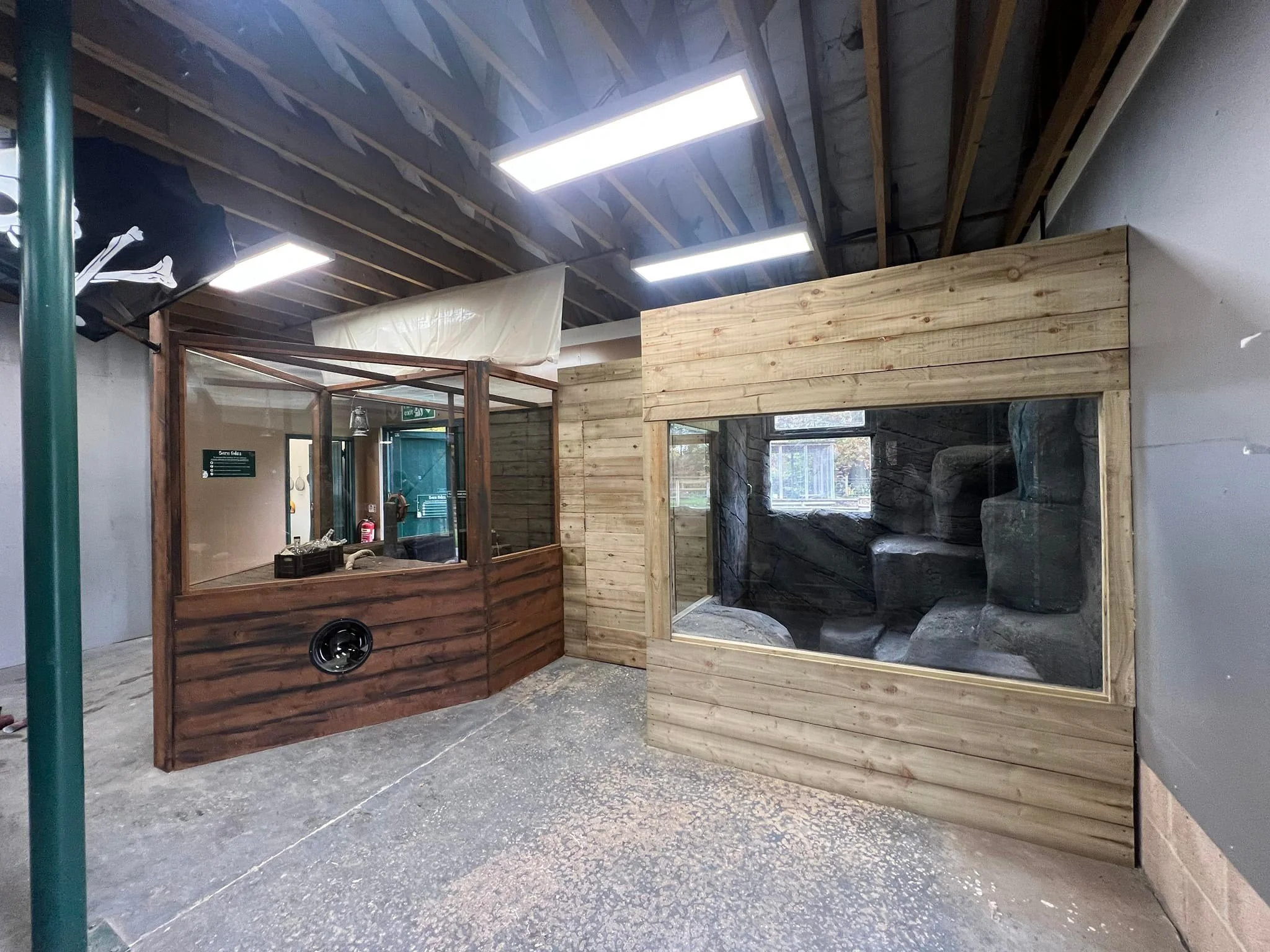 Indoor construction area with wooden and glass structures, including a small wooden enclosure with rocks inside and some construction materials on the floor.