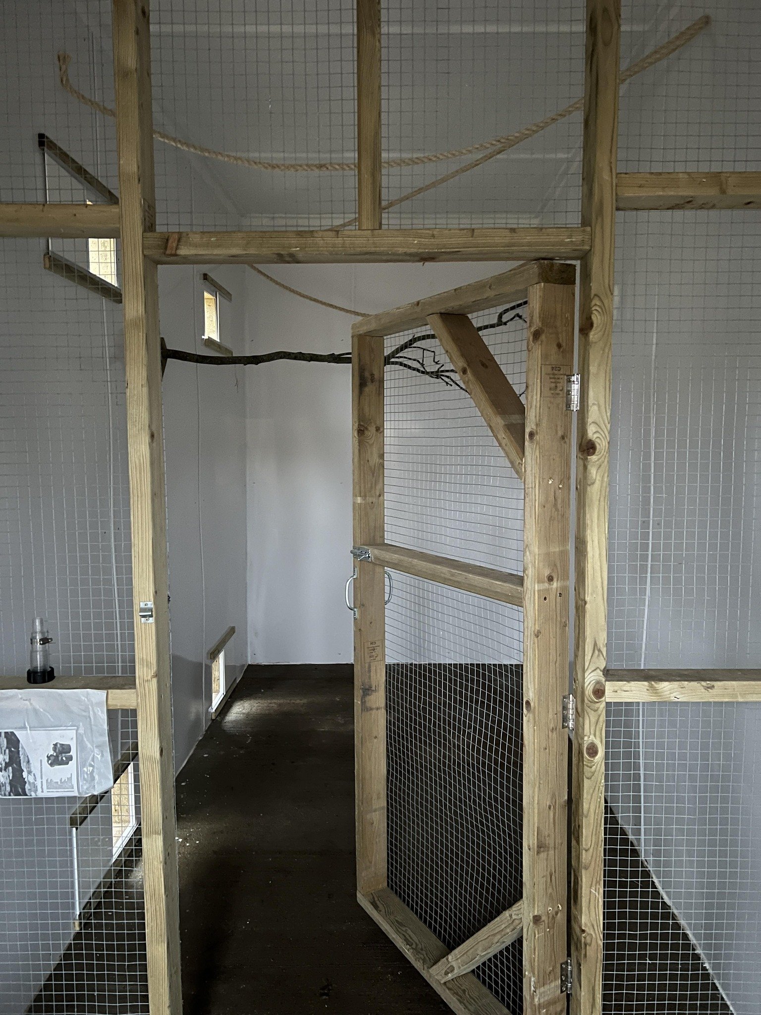 Partially constructed indoor enclosure with wooden framing and wire mesh walls, likely for small animals or pets.