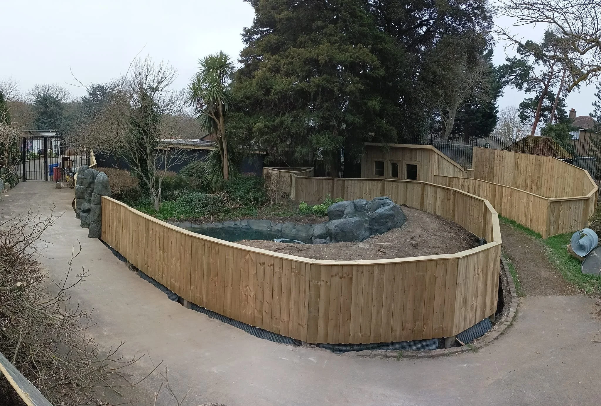 A backyard with a newly built wooden fence around a small pond with rocks, trees, and a pathway.