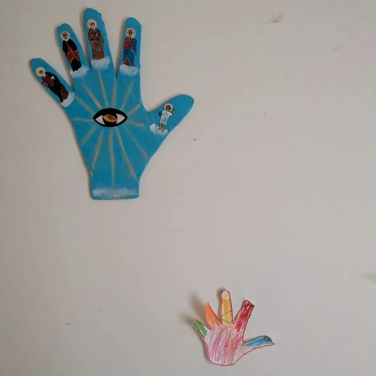 Colorful paper hand cutouts on a wall, with religious and eye symbols, representing spiritual or religious artwork.