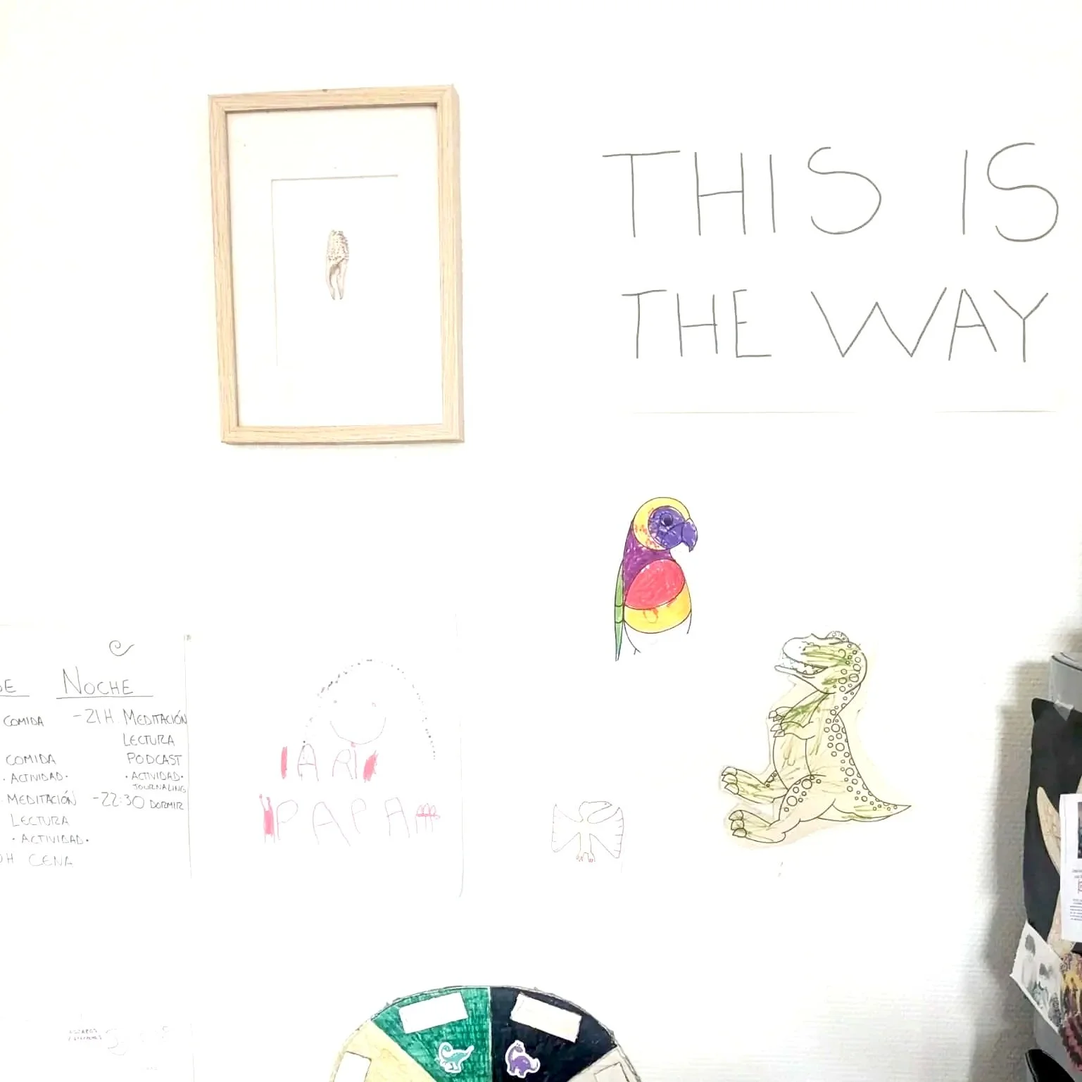 White wall with framed drawing, colorful parrot illustration, and doodles of a dinosaur, a butterfly, and words 'THIS IS THE WAY' written in large letters.