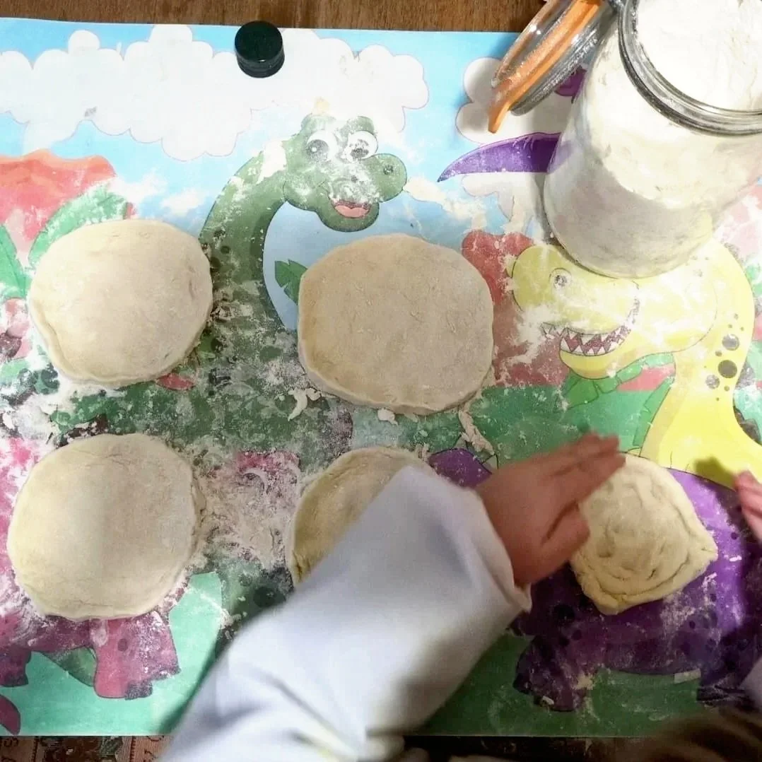 Child shaping dough into balls on a colorful dinosaur-themed table.