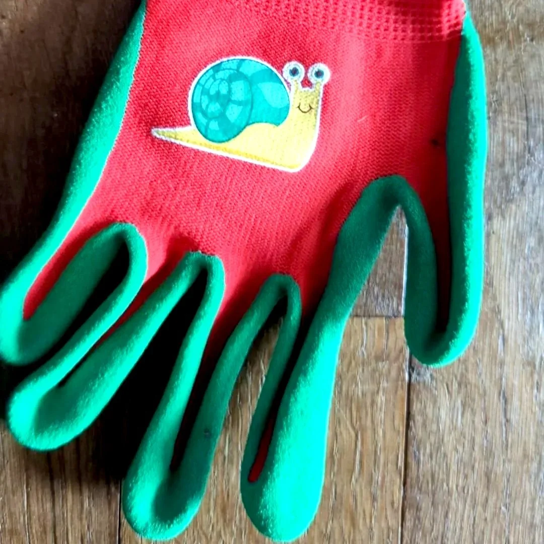 A red gardening glove with green trim and a snail cartoon patch on the back, lying on a wooden surface.