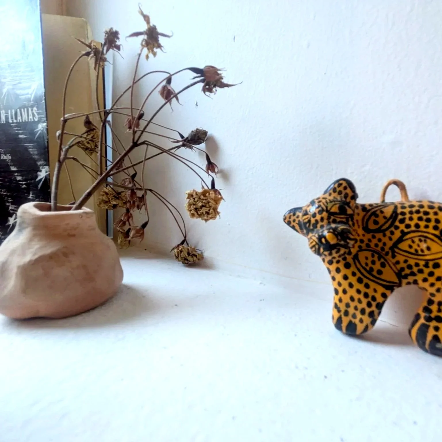 Dried flower bouquet in a ceramic vase on a white surface, with a decorative yellow and black leopard figurine on the right.