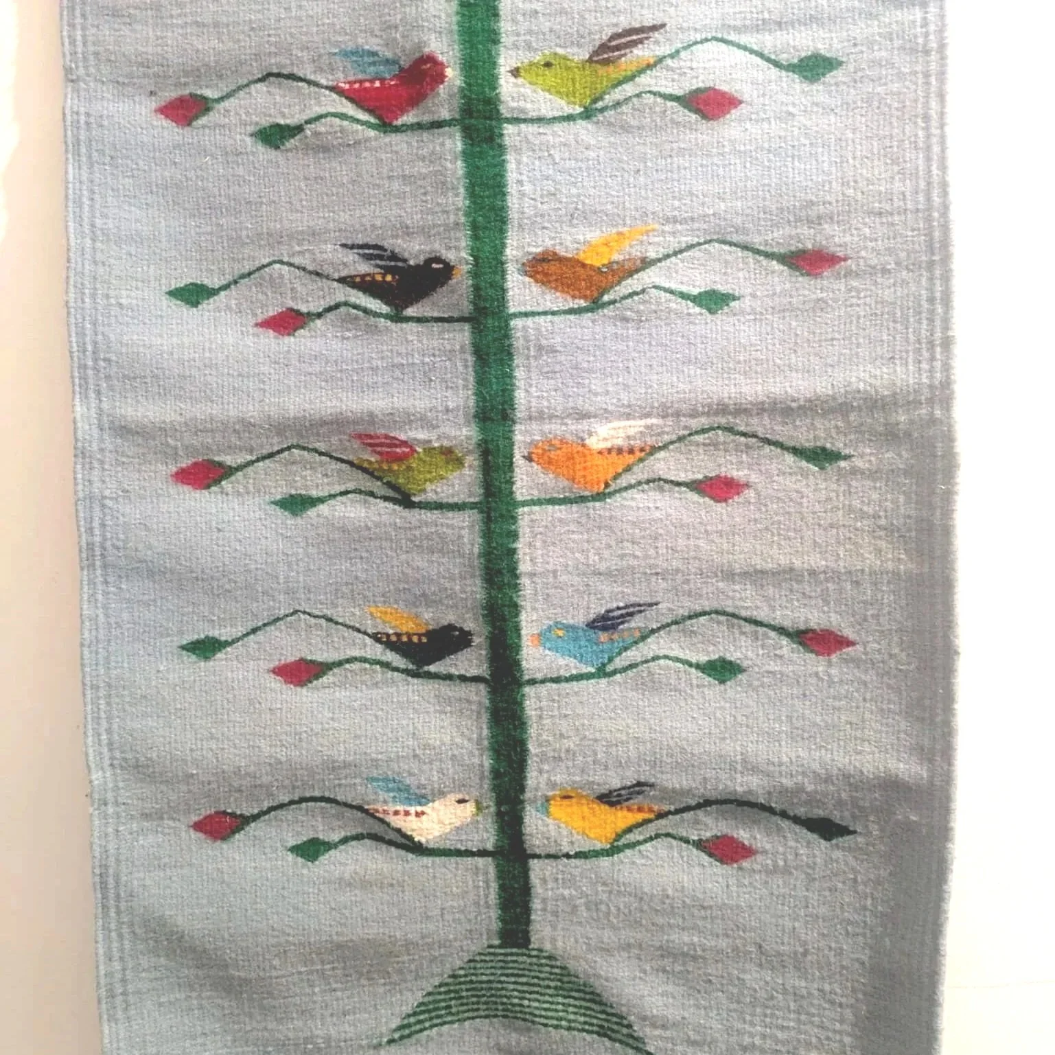 A textile wall hanging with embroidered colorful birds perched on green wavy lines, arranged in four rows on a white background.