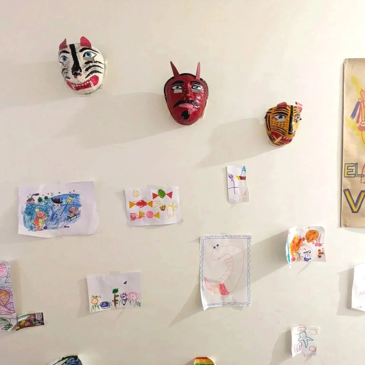 Wall decorated with three colorful masks and children's drawings of various subjects.