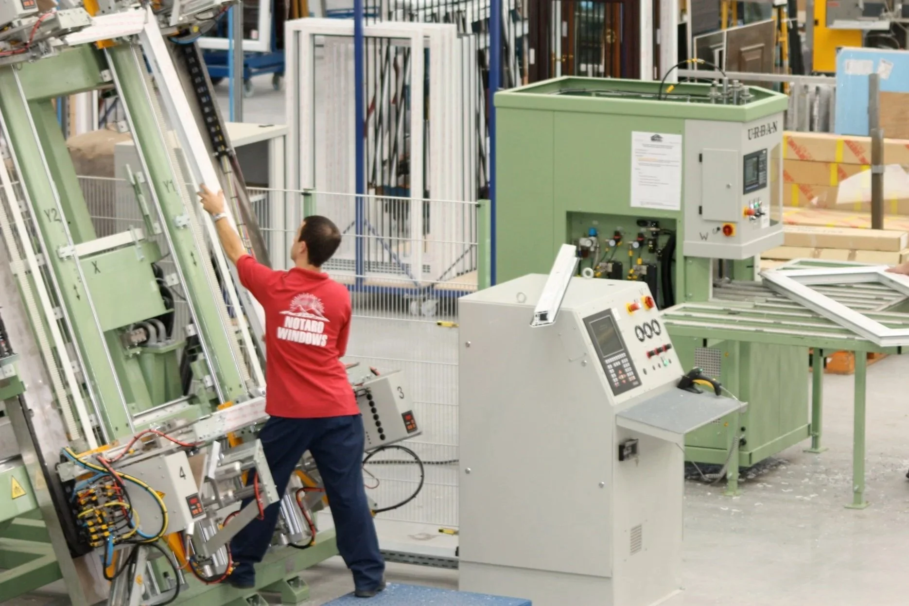 A worker tests and assembles window frames with specialized machinery in a factory.