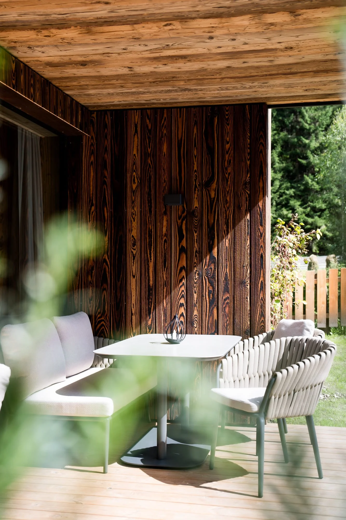 Ein Außenbereich mit einem weißen runden Esstisch, umgeben von weißen, flechtartigen Stühlen auf der Terrasse der SLOW Chalets