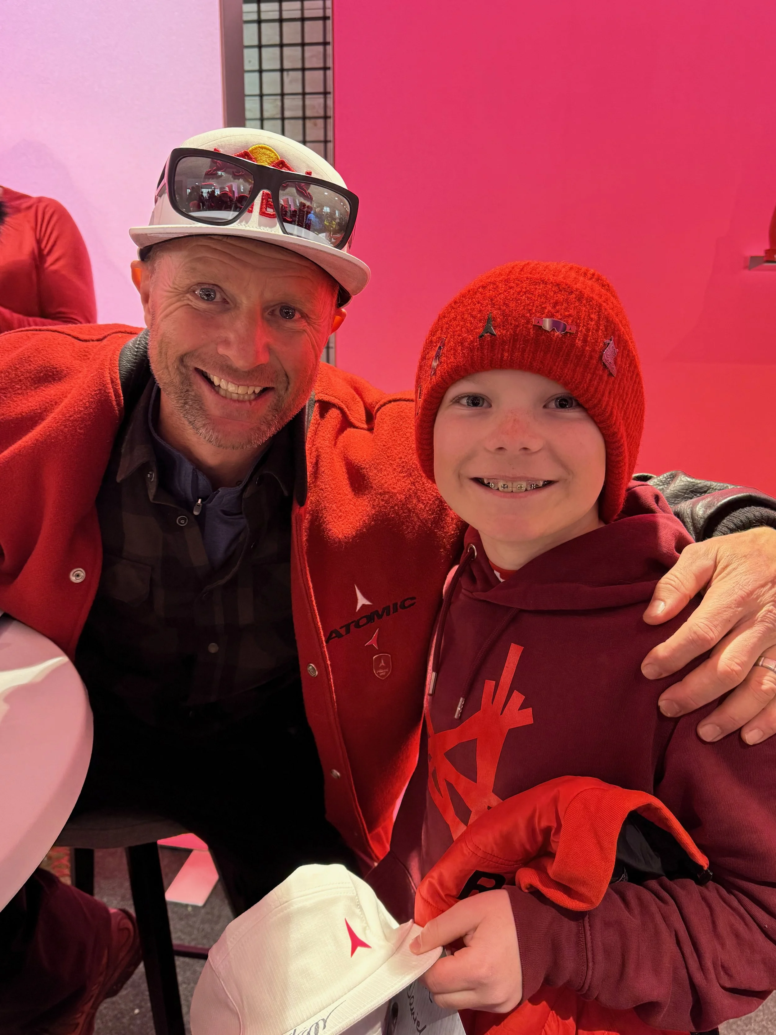 Daren Rhalves, former Kitzbuel downhill winner, standing next to Daniel Fatzinger in Saalbach, Austria, taking a selfie together in a pink-lit room.