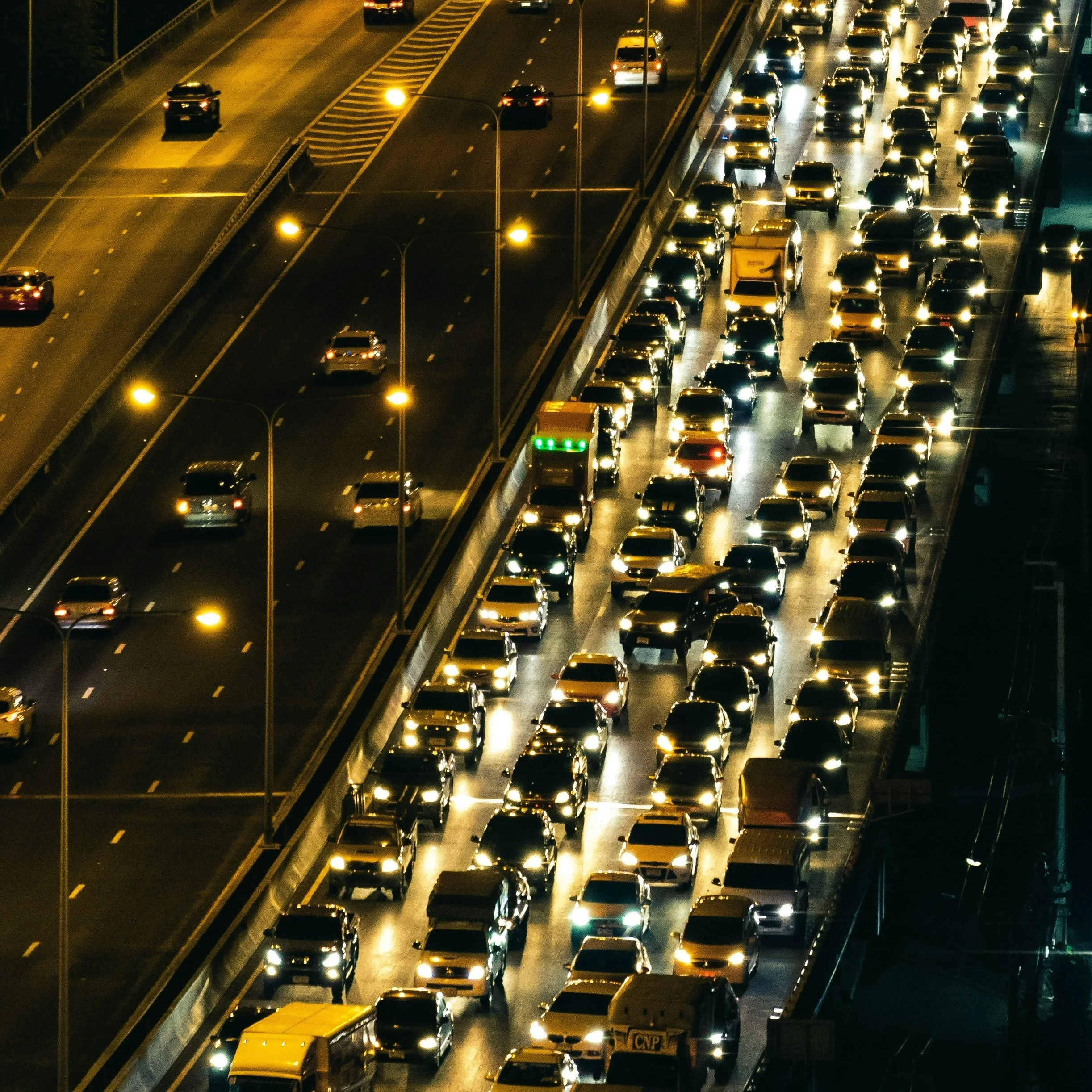 Verkehr auf einer vielbefahrenen Straße bei Nacht mit vielen Autos und Straßenlaternen, einige Fahrspuren sind stockend, andere frei.