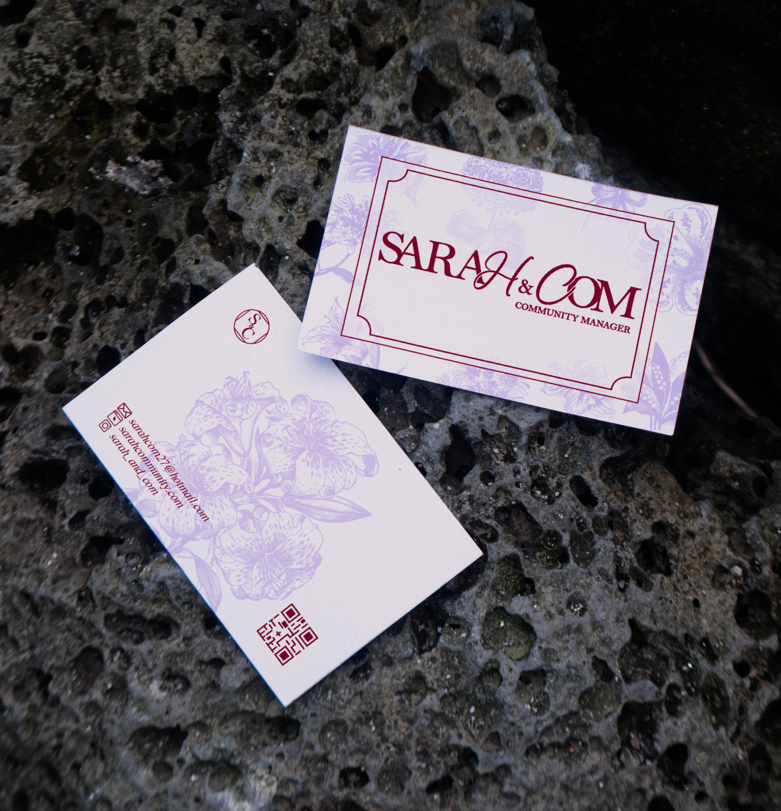 Cartes de visite avec le nom SARAH & COM et la mention Community Manager, posées sur une surface rocheuse