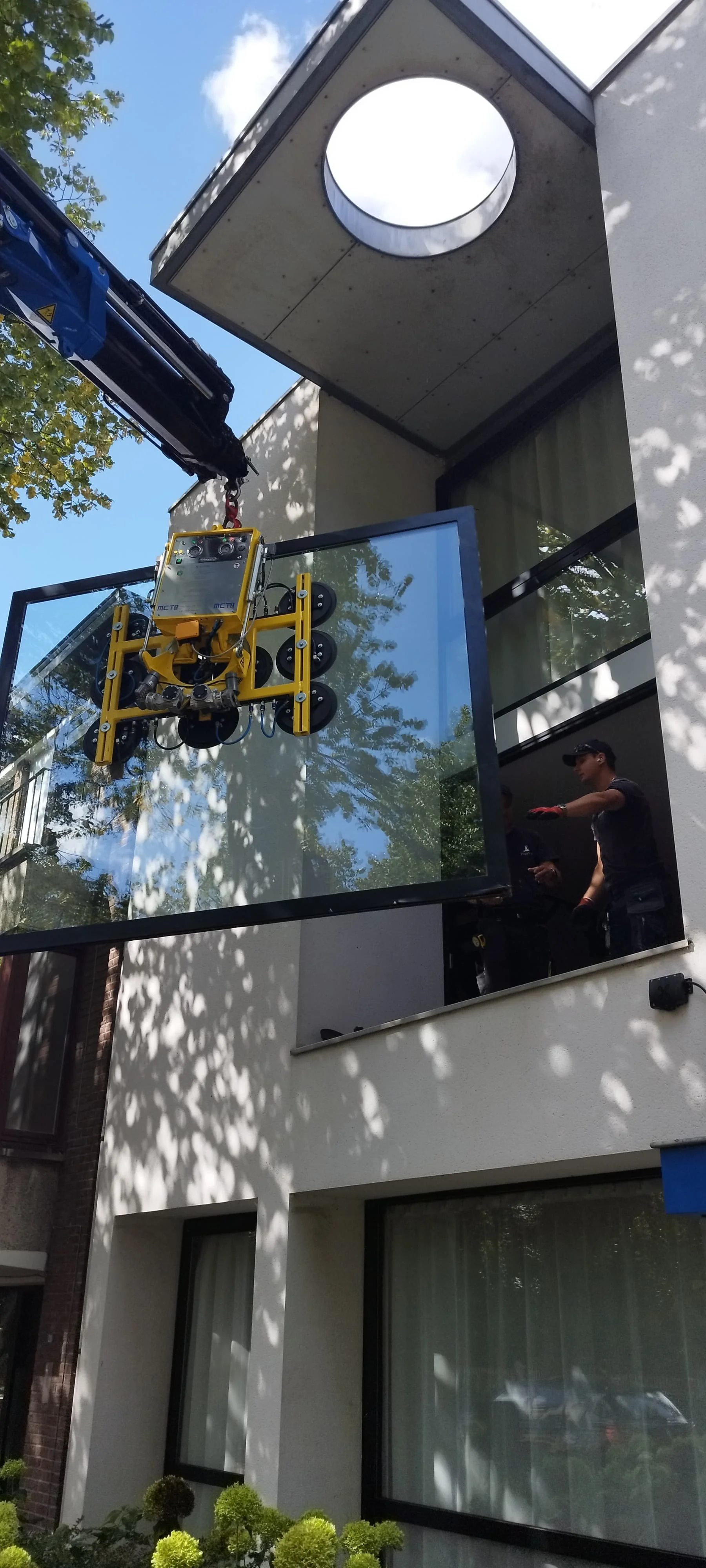 Het installeren van een grote glazen raam op het balkon van een modern wit gebouw met twee verdiepingen.