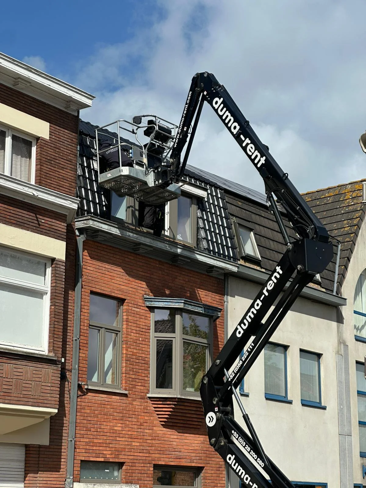 Werknemers gebruiken een hoogwerkersplatform om werkzaamheden uit te voeren op het dak van een appartementsgebouw.