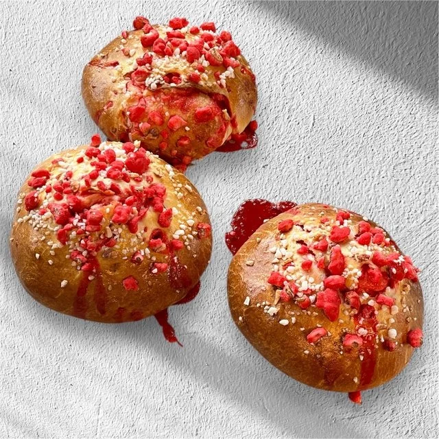 Trois brioches décorées de sucre coloré, de confiture de fraise et de petites perles de sucre, sur une surface blanche.