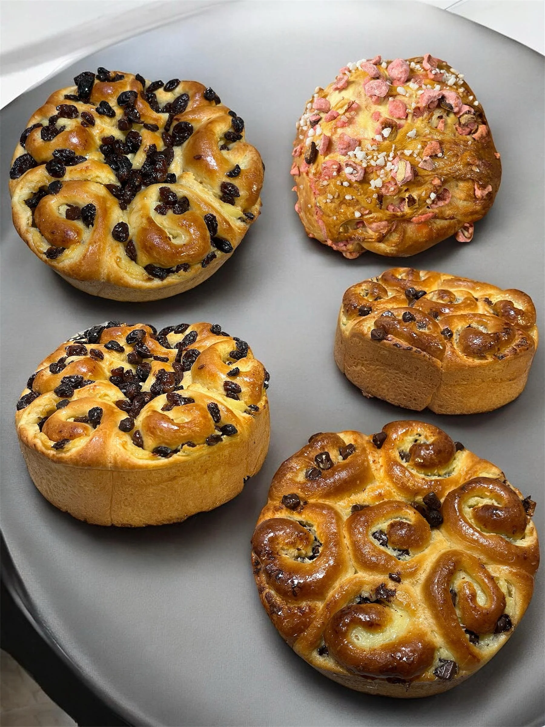 Gâteau brioché avec des pépites de chocolat, certains décorés avec des fruits confits ou des fruits secs, disposés sur une assiette grise.