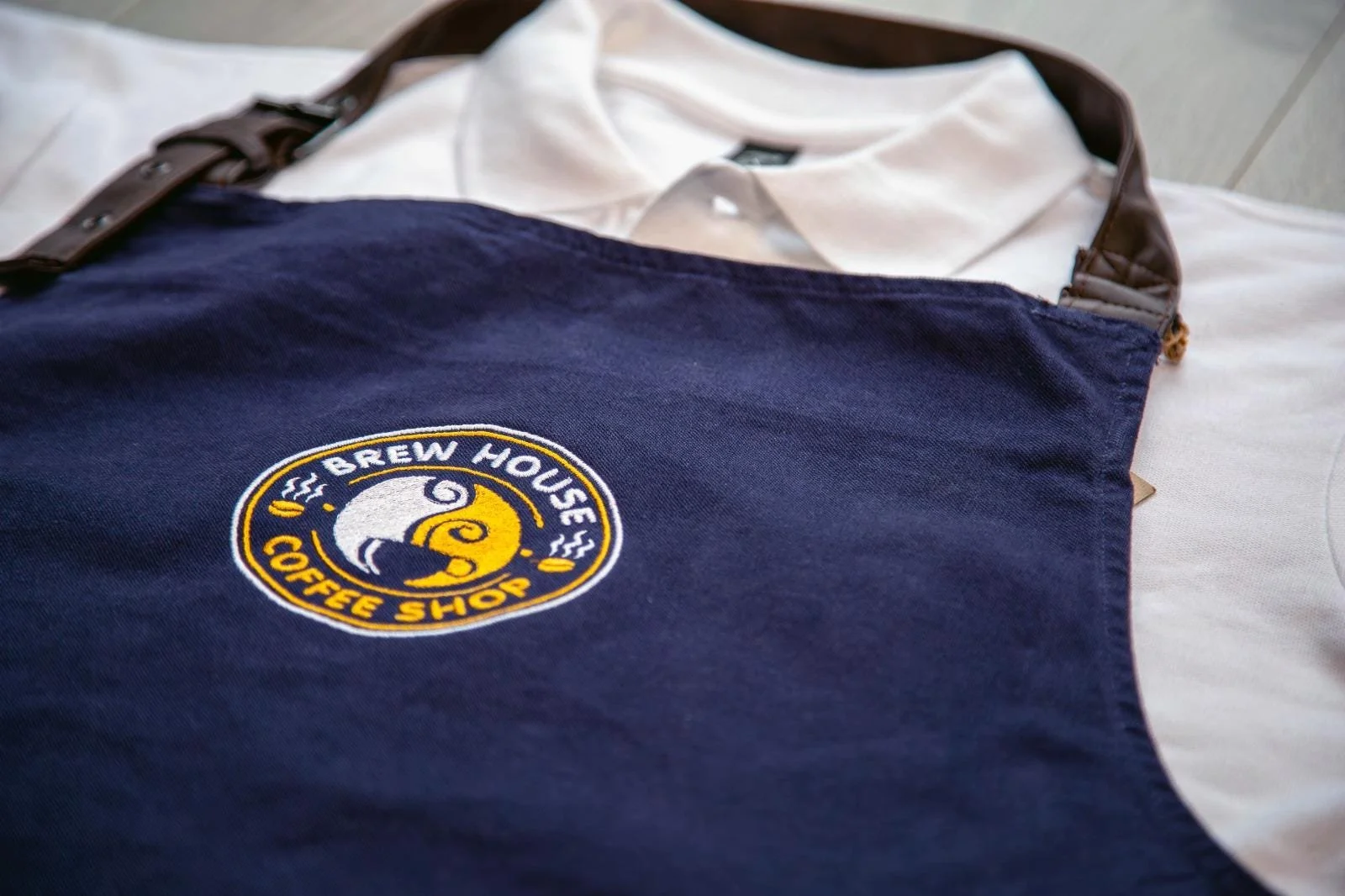 An apron with the Brew House Coffee Shop logo lying on a white shirt.