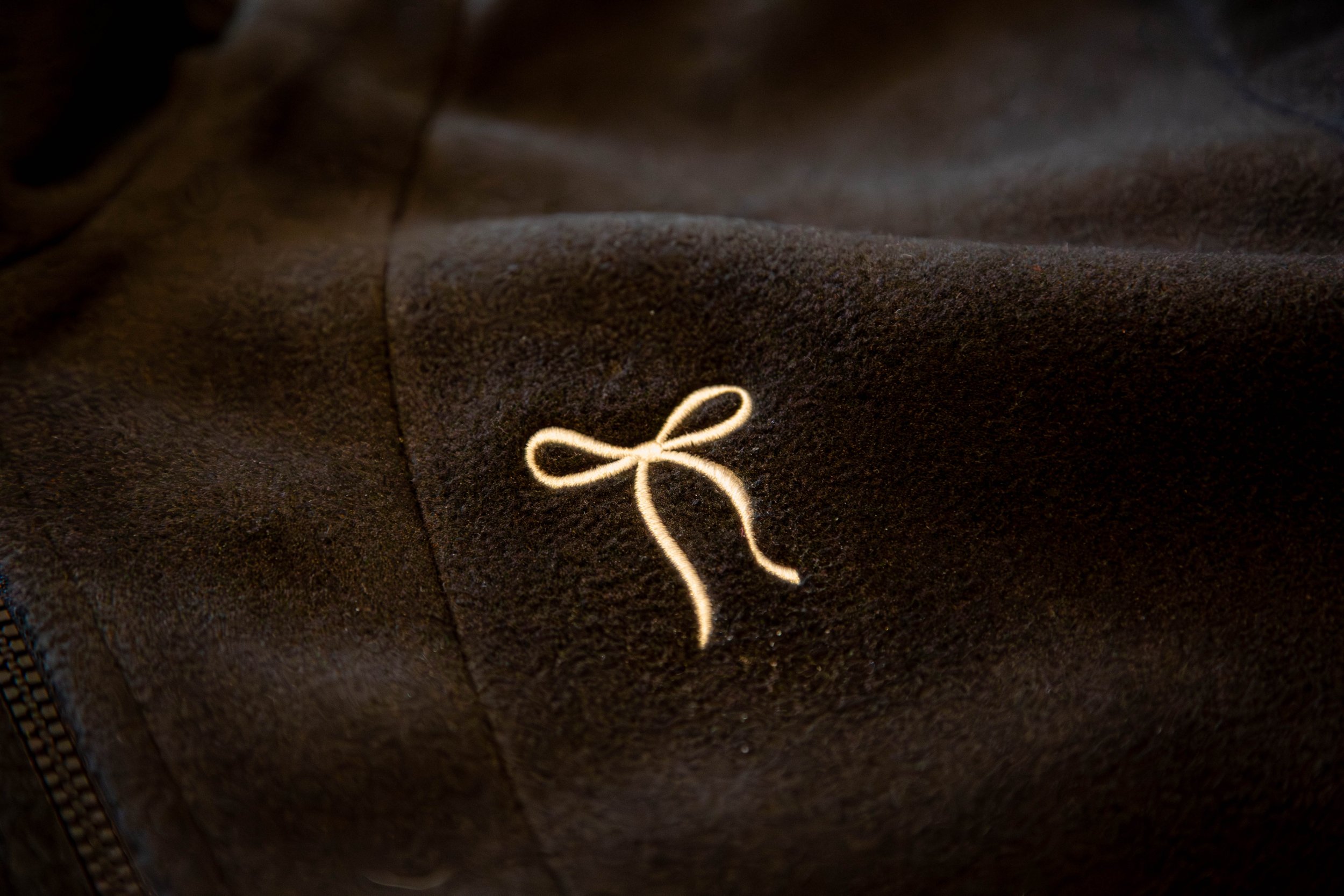 Close-up of dark brown fabric with a small embroidered beige bow.