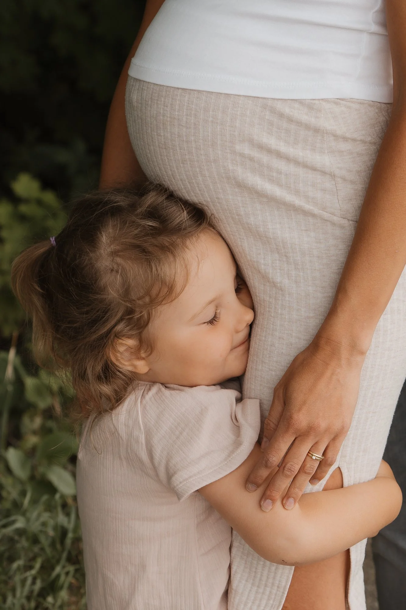 Ein Kind umarmt den Bauch einer schwangeren Frau, fühlt sich geborgen und glücklich.