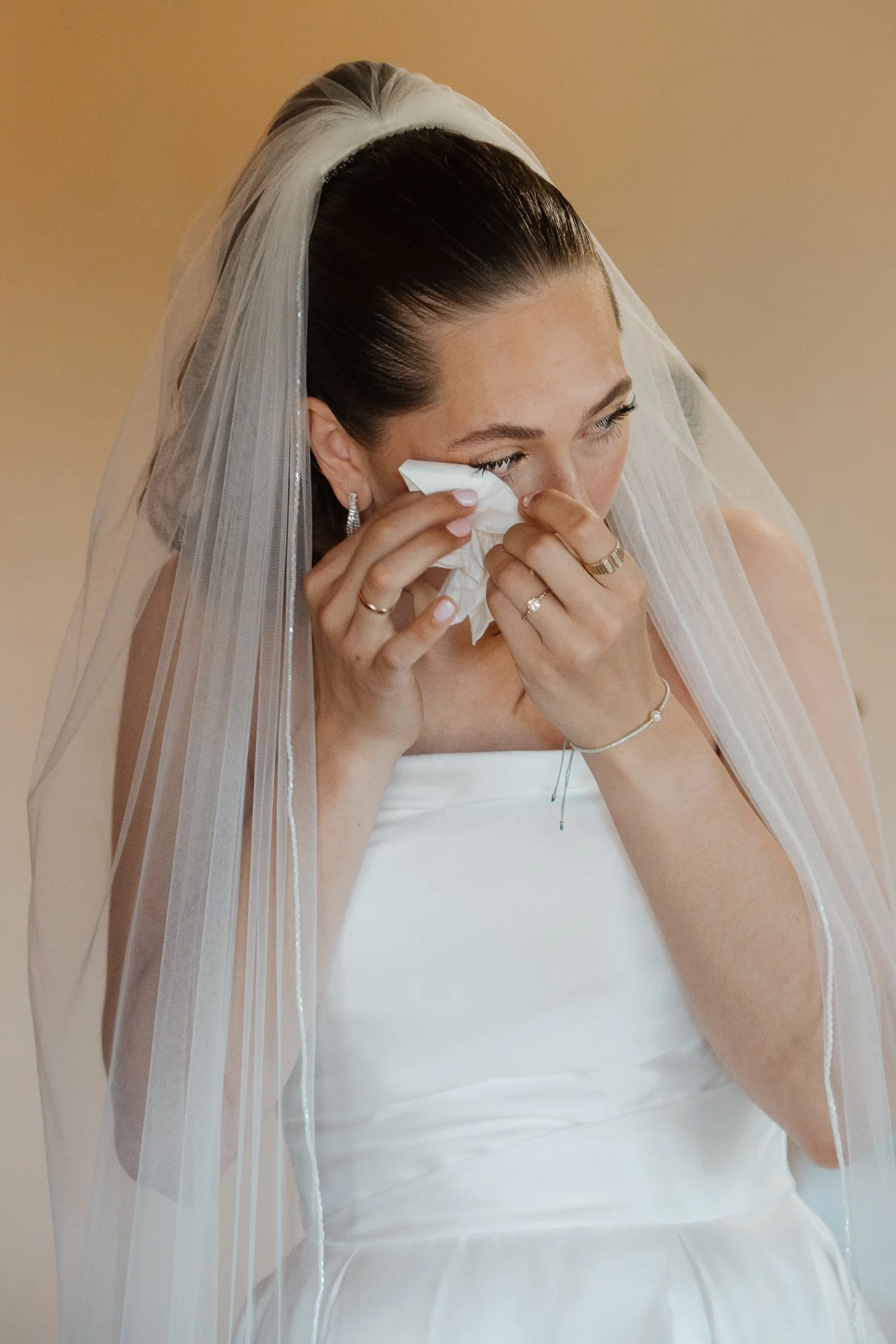 Braut trägt ein weißes Hochzeitskleid mit Schleier und wischt sich die Tränen des Glücks ab.