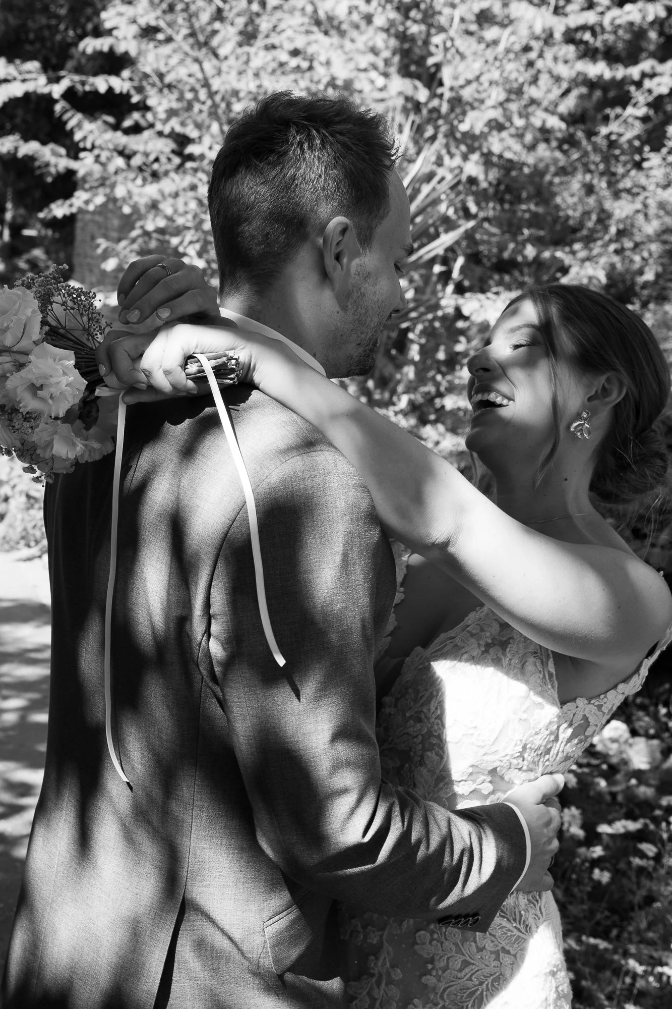 Ein glückliches Brautpaar, umarmt und lächelnd, während sie im Freien bei Sonnenlicht fotografiert werden, schwarz-weiß