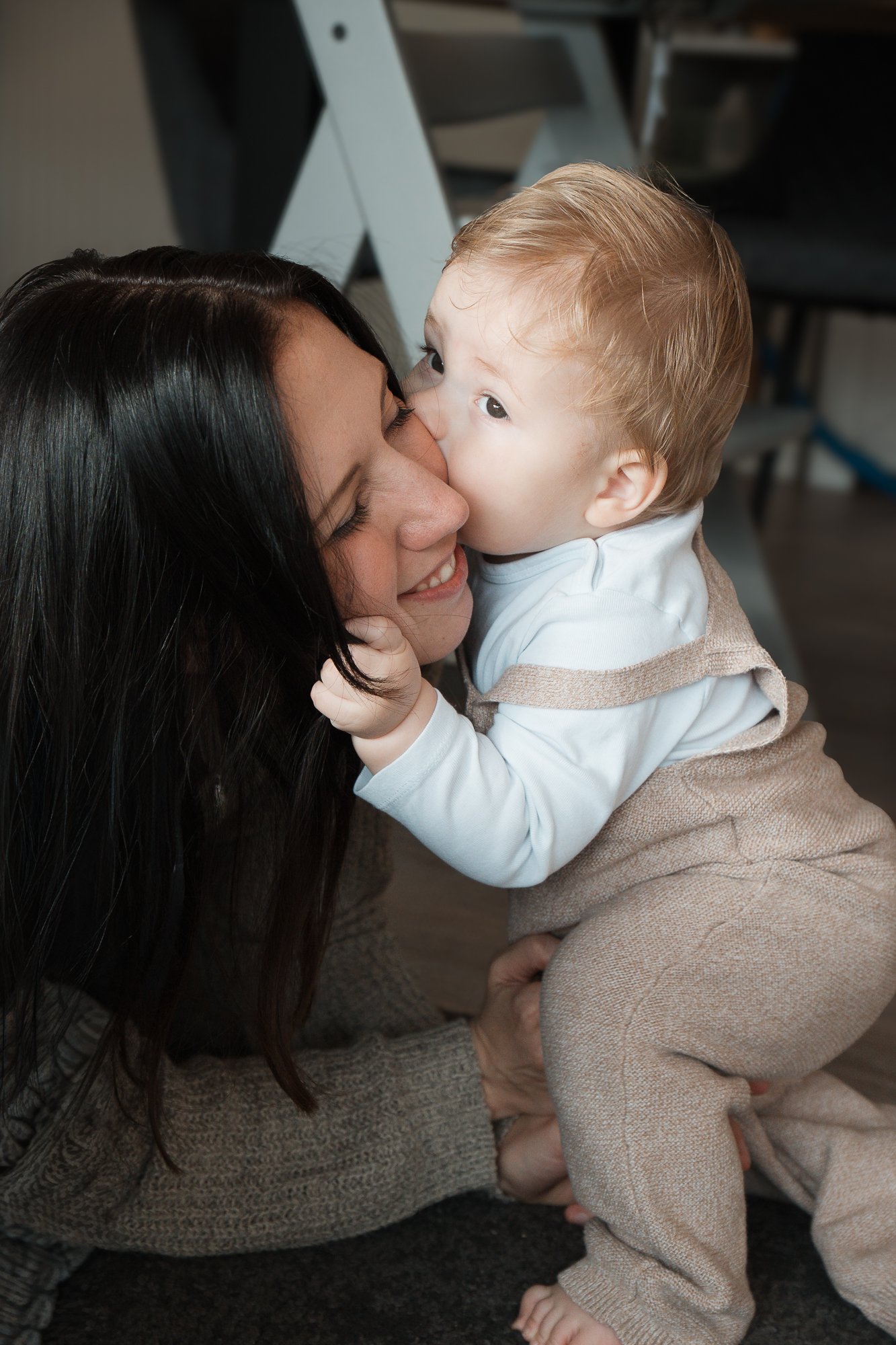 Eine Frau und ein Kleinkind, das sie küsst, auf dem Boden sitzend.