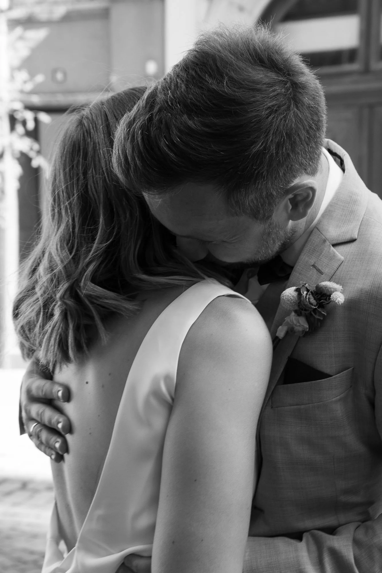 Zwei Personen, die sich auf einer Hochzeit umarmen, in Schwarz-Weiß, emotionale Nähe, formale Kleidung, ein Mann in einem Anzug mit Blumenboutonnière, eine Frau in einem Kleid mit schulterfreiem Schulterteil.