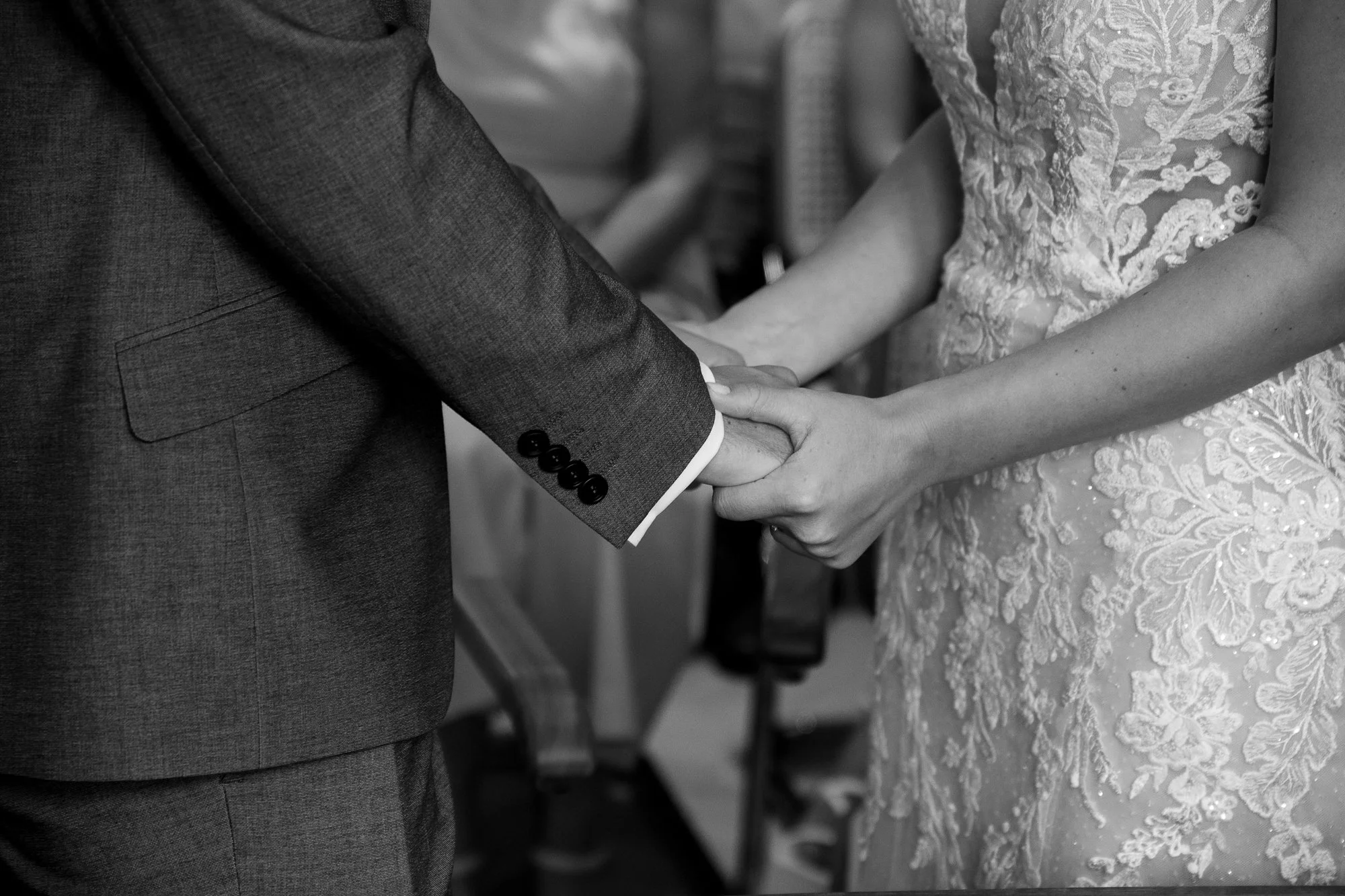 Nahaufnahme eines Brautpaares, das sich die Hände hält, bei einer Trauung, im Schwarz-Weiß-Format.