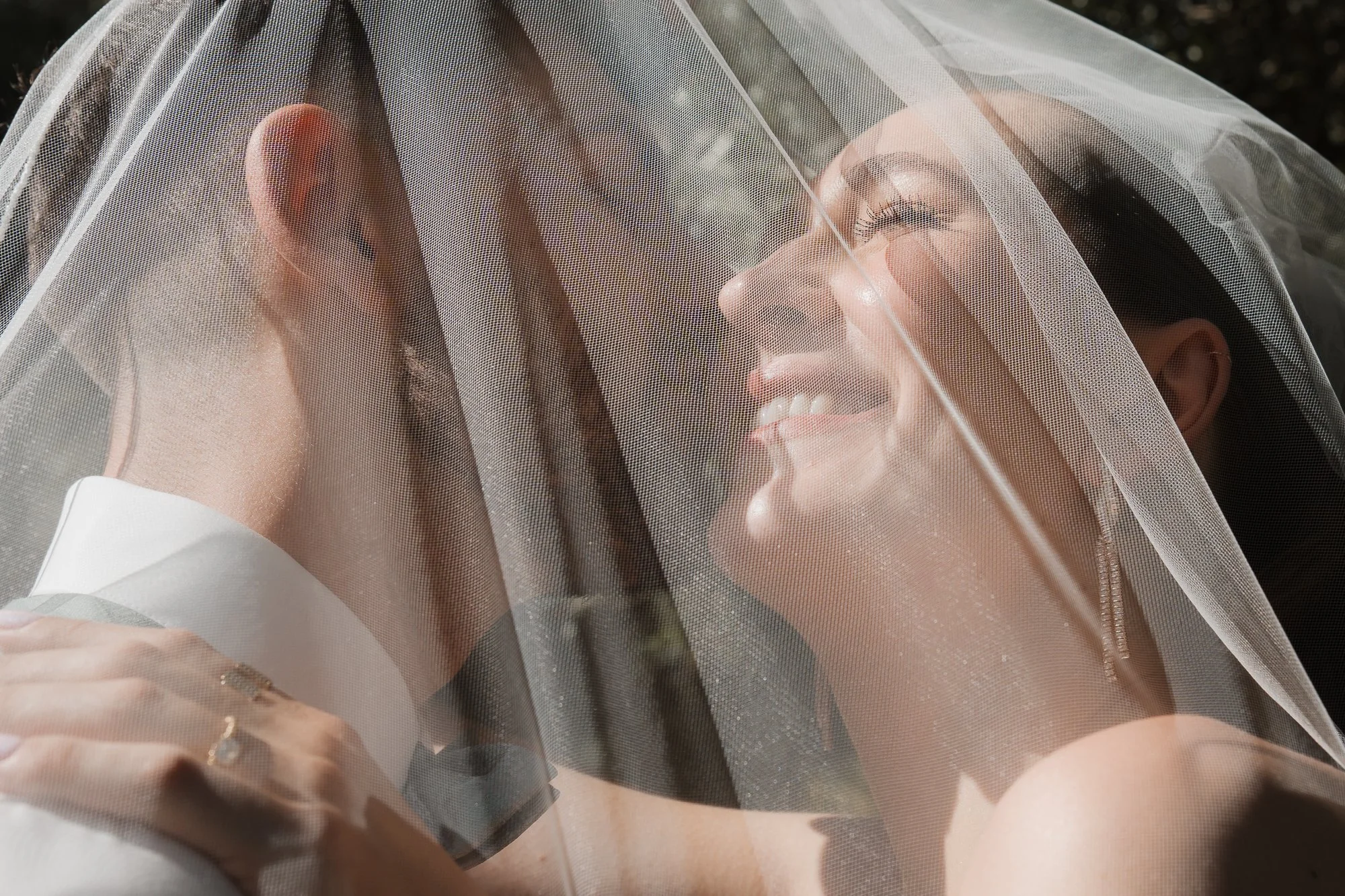 Verliebtes Brautpaar unter einem Schleier, lachend und in einer Umarmung