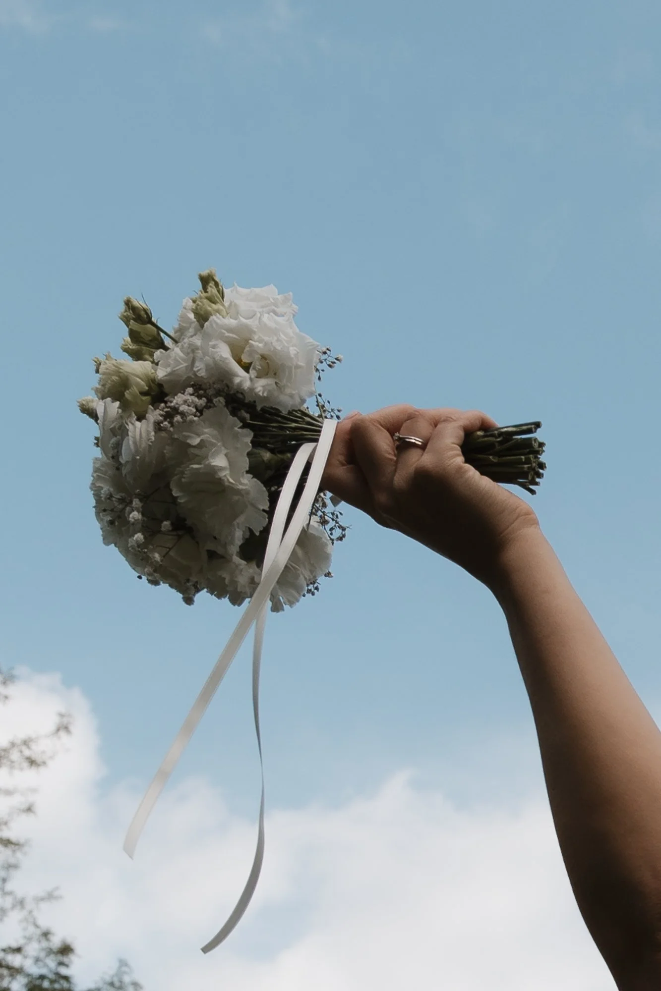 Hand hält einen Strauß weißer Blumen gegen den Himmel.
