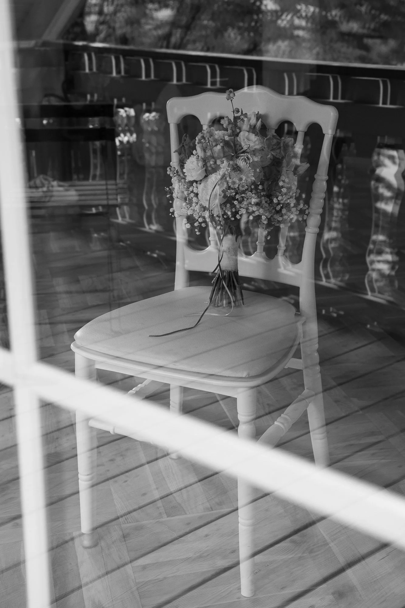 Ein Blumenstrauß auf einem weißen Stuhl, reflektiert in einem Fenster.