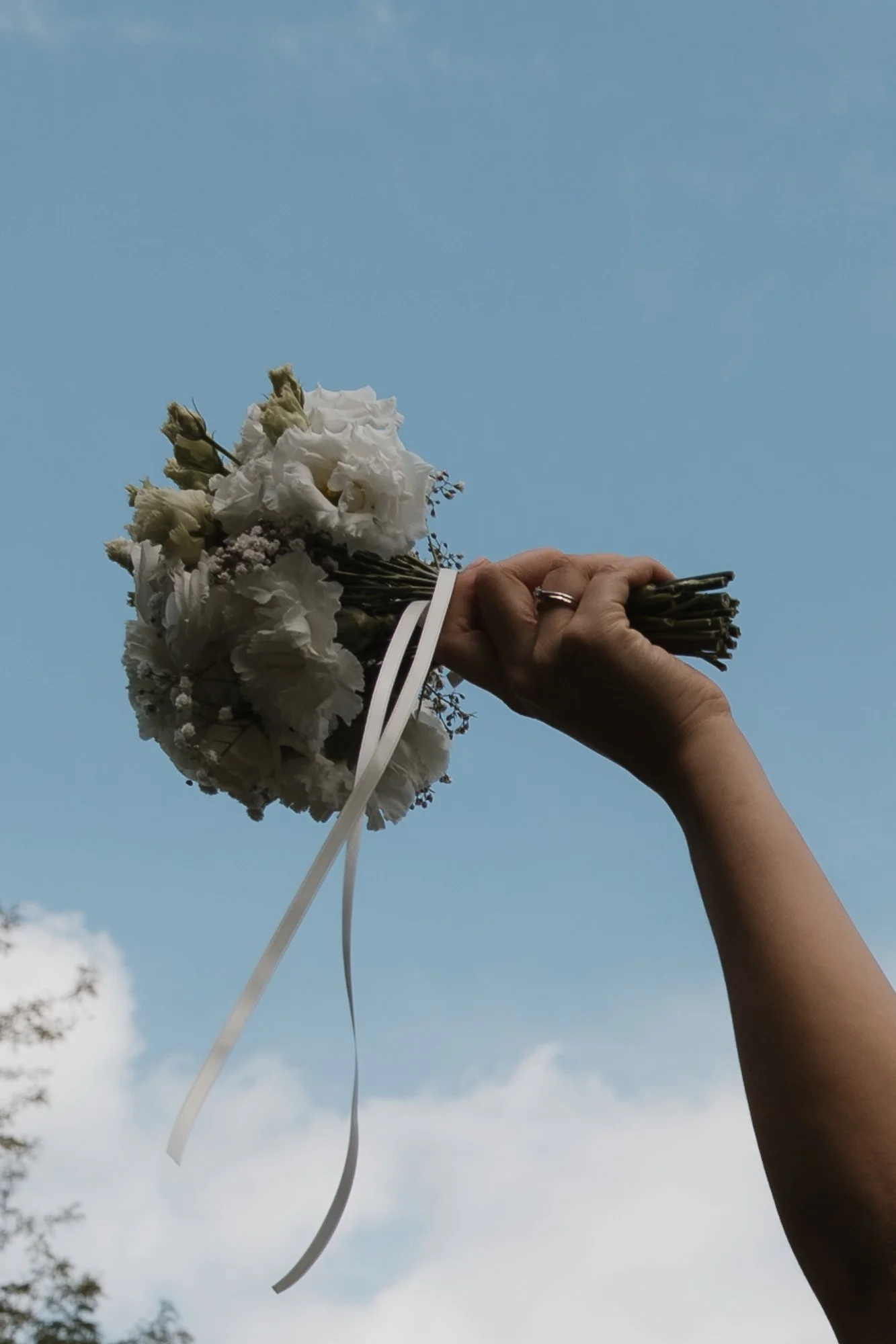 Ein Hand hält ein Brautstrauß aus weißen Blumen gegen den Himmel.