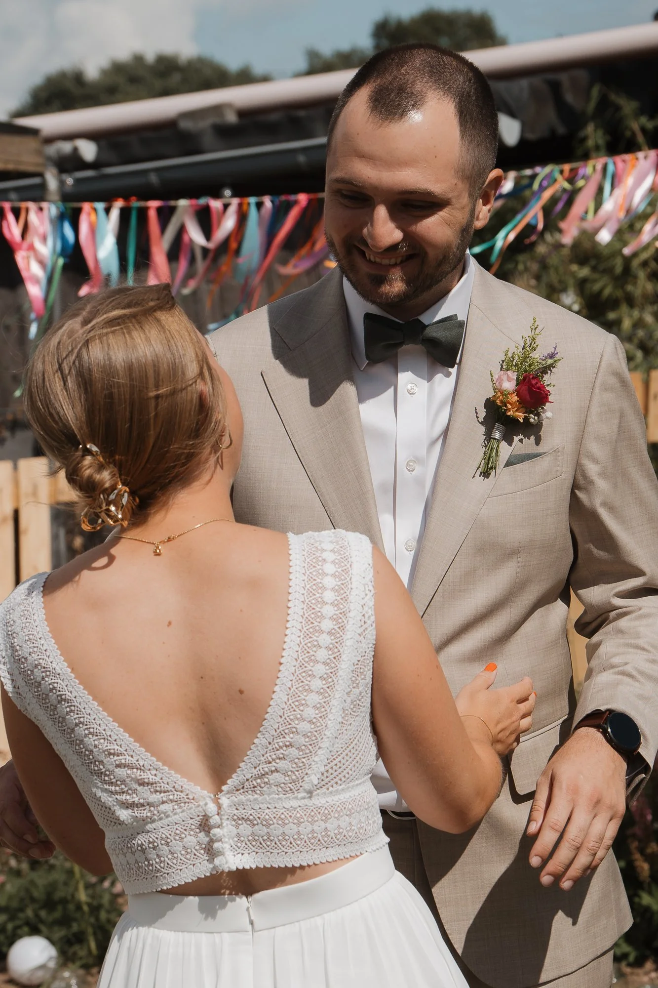 Ein Brautpaar bei einer Hochzeit, vermutlich beim ersten Tanz, draußen bei Sonnenlicht, mit bunten Dekorationen im Hintergrund.