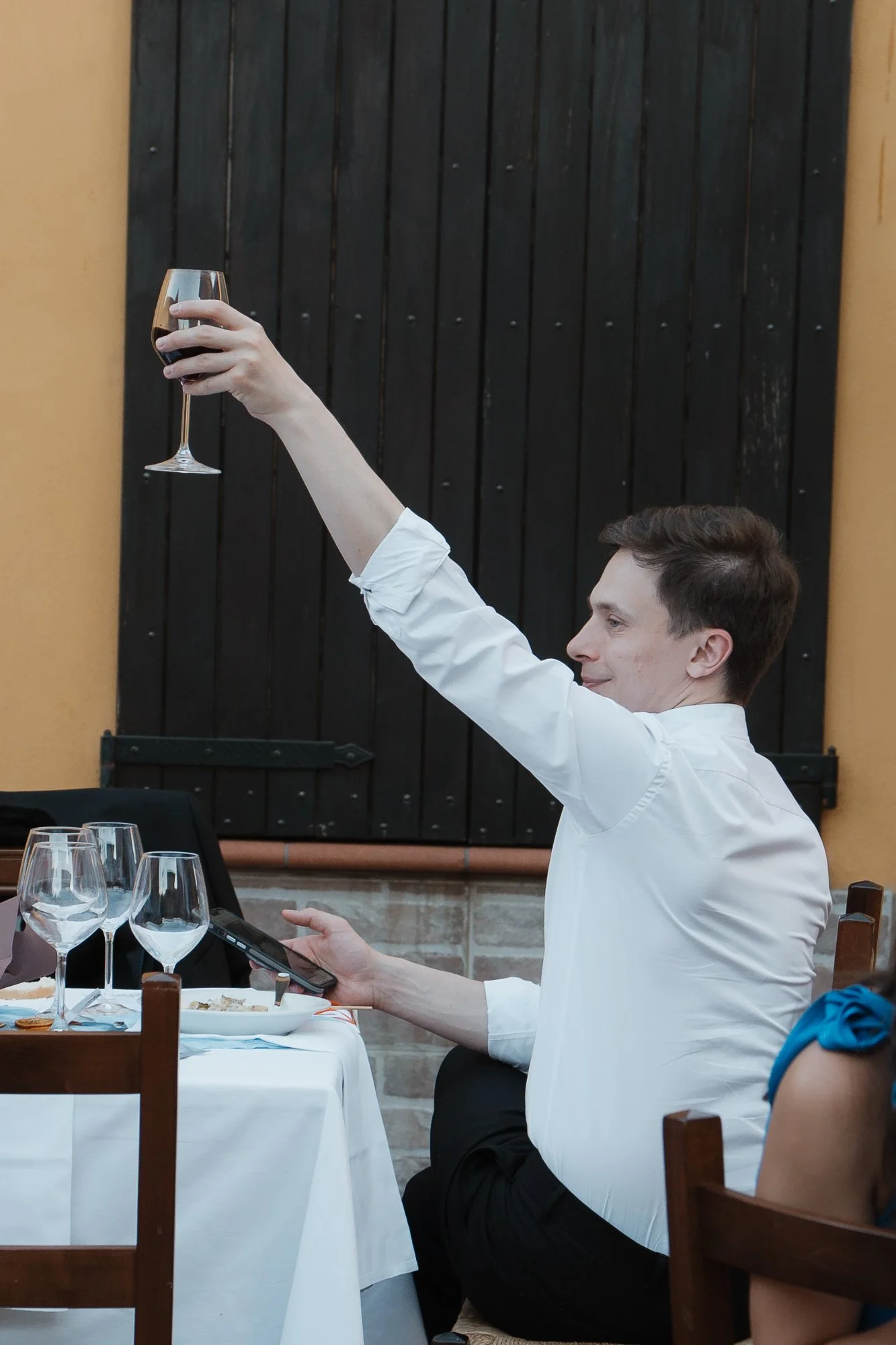 Ein Mann in weißem Hemd hebt ein Weinglas in einem Restaurant hoch.