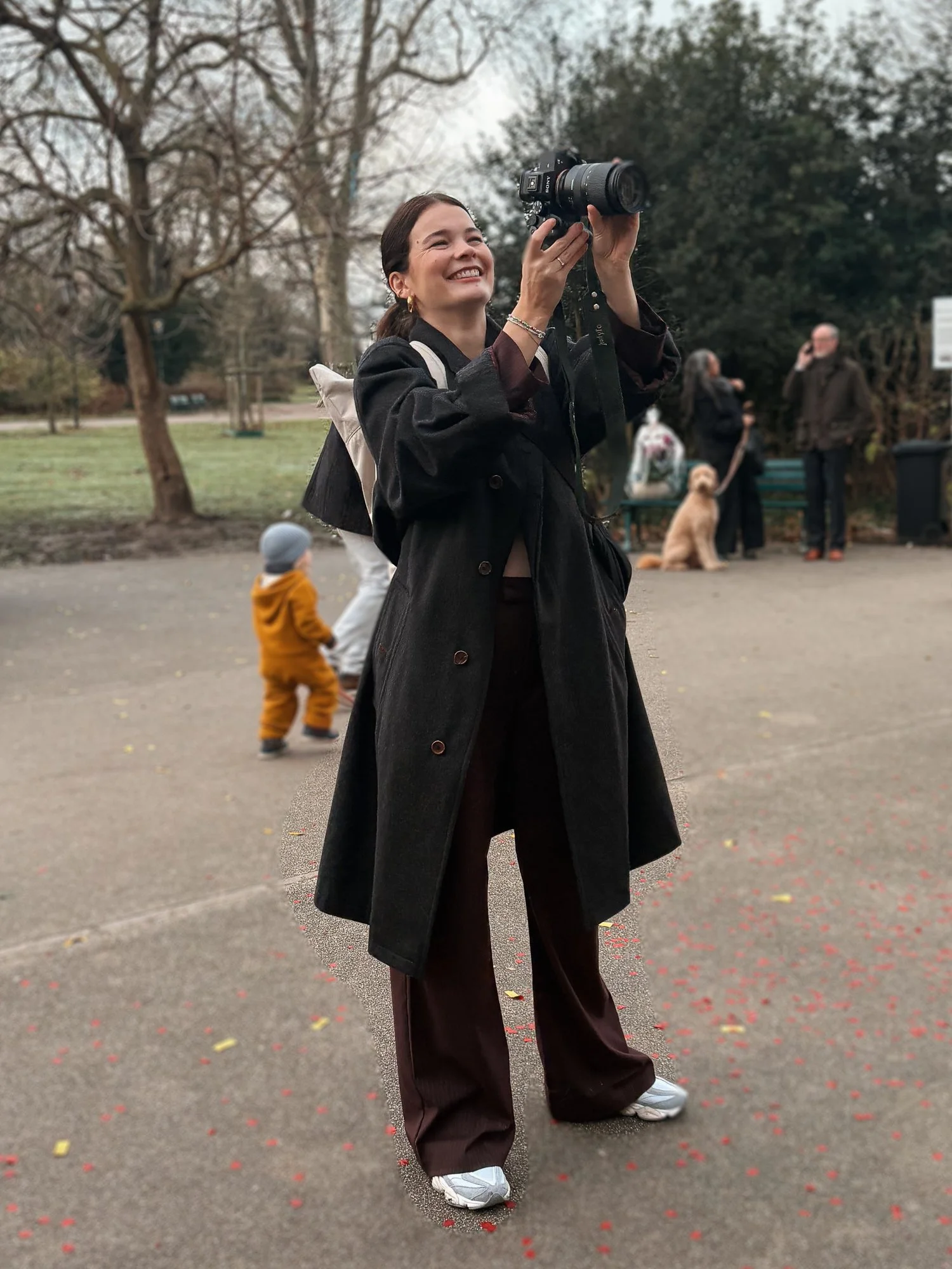 Junge Frau mit einer Kamera in der Hand, lachend und im Freien in einem Park.