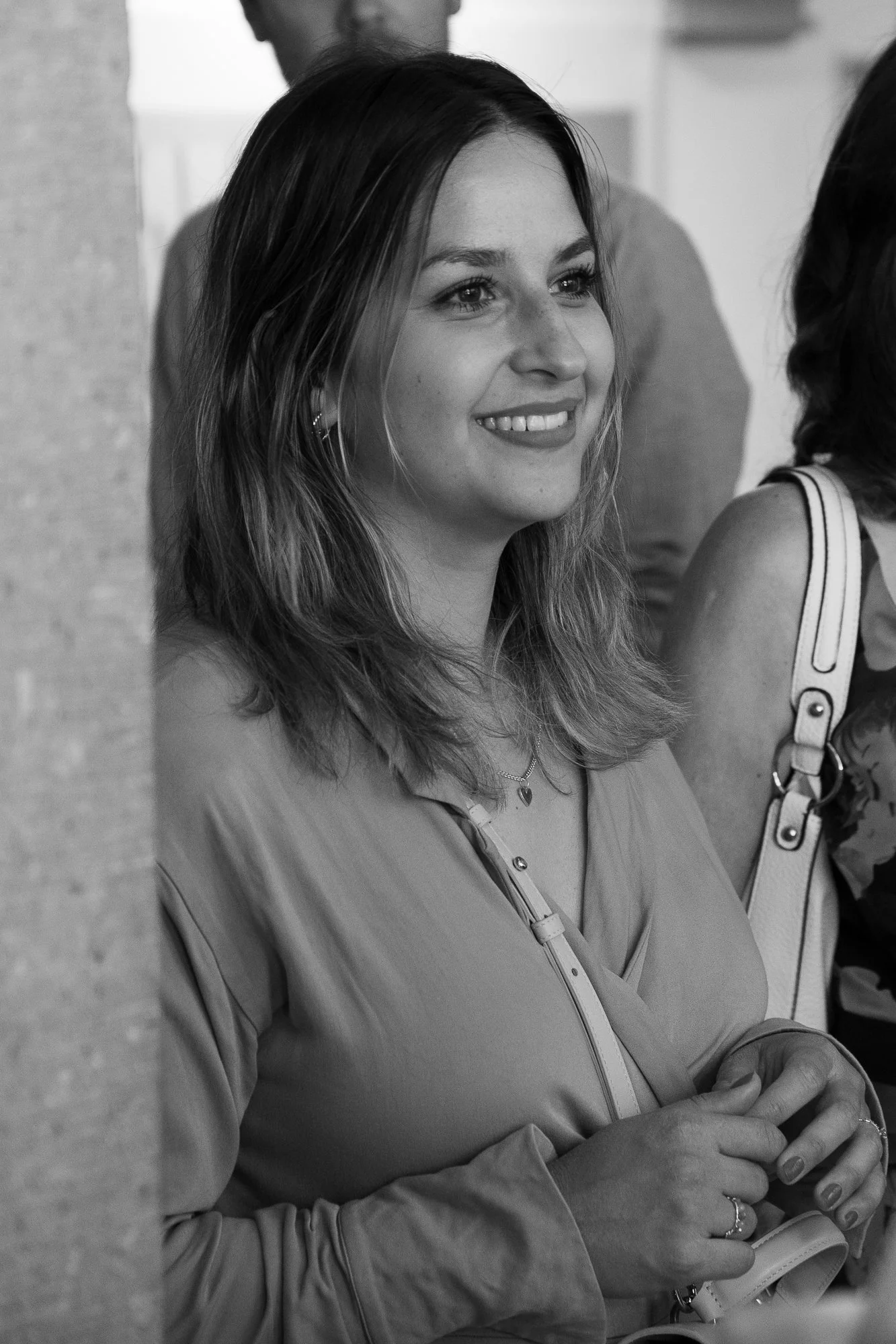 Schwarz-weiß-Foto einer lächelnden jungen Frau mit Schulterlänge Haaren, die einen dünnen Ring am Finger trägt, in einer Gruppe.