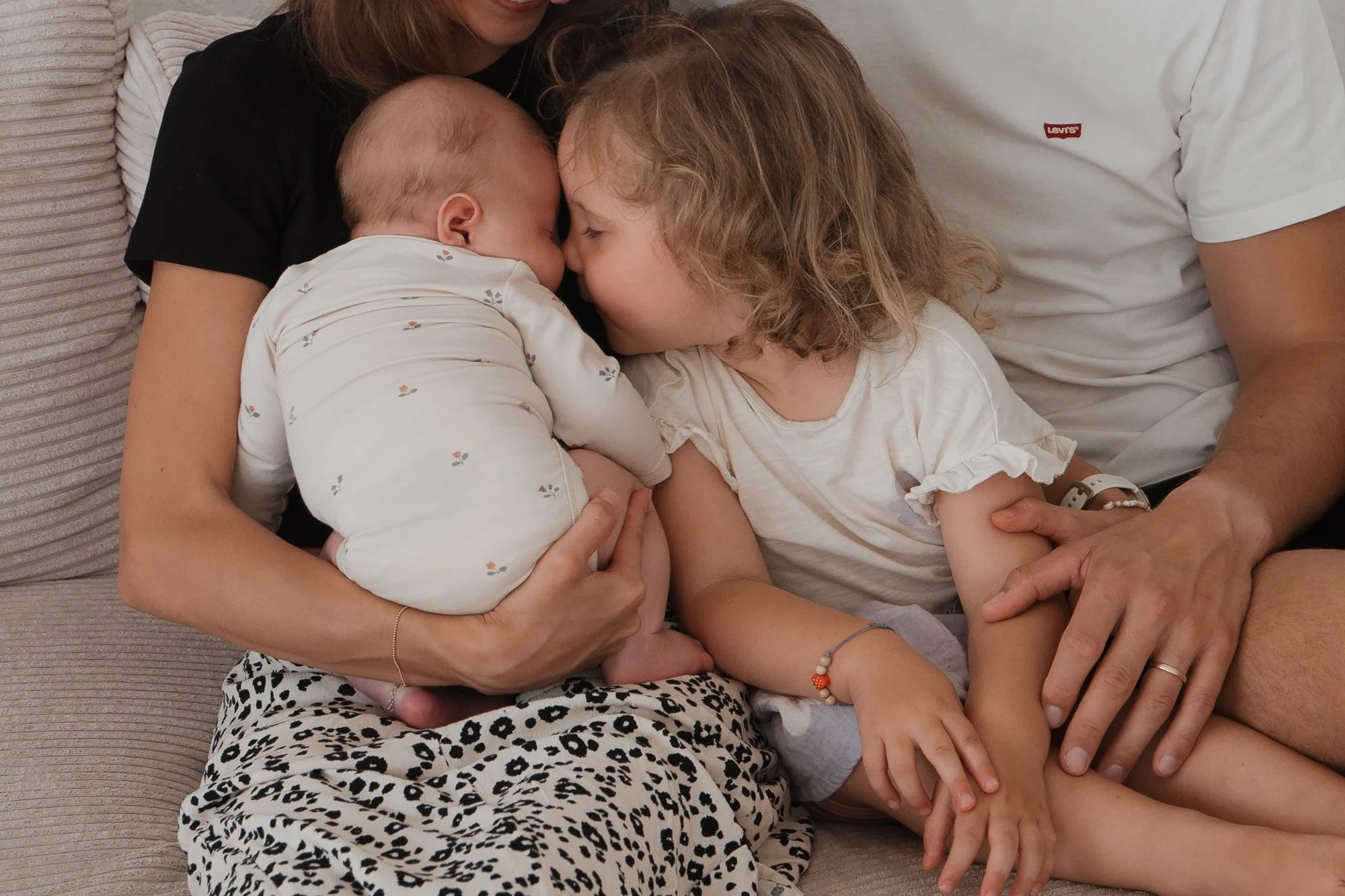 Eine Familie mit einem Baby, einer jungen Tochter und Eltern, die auf einem Sofa sitzen und sich mit den Nasen berühren.