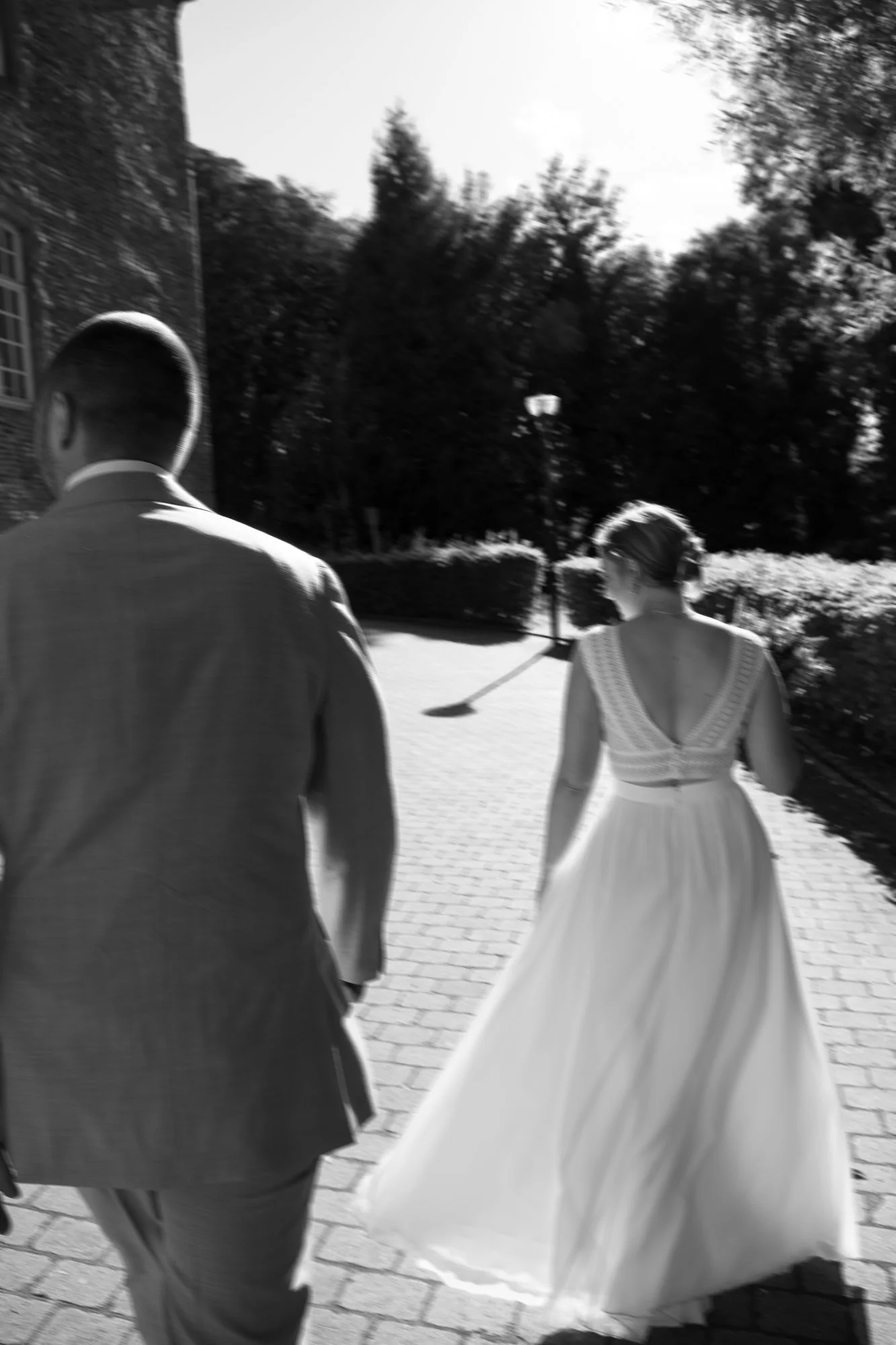 Ein Mann in Anzug und eine Frau in einem weißen Brautkleid gehen auf einem gepflasterten Weg.